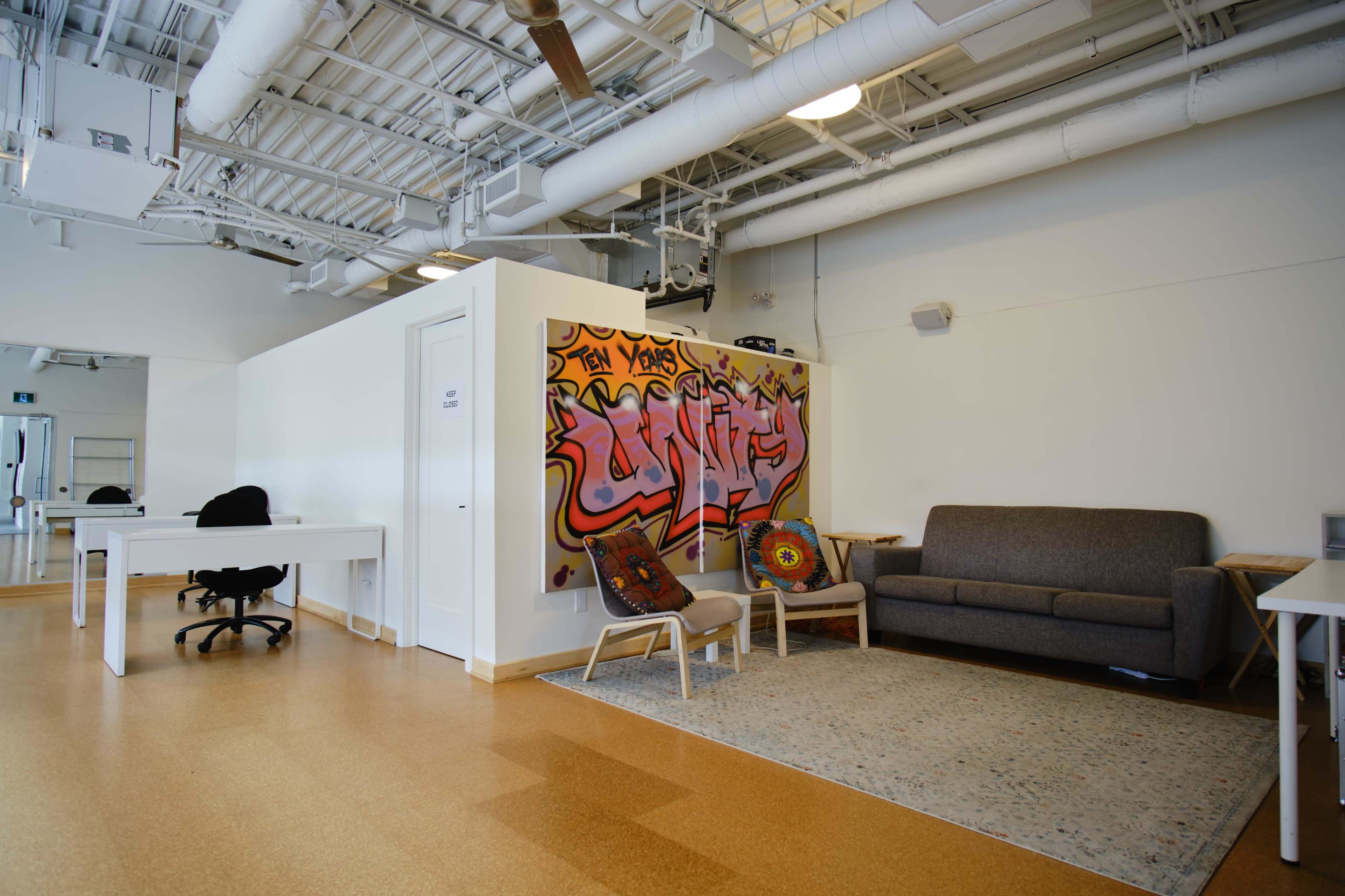 A modern office space features a gray sofa, two chairs, a decorative rug, and a wall with colorful graffiti art.