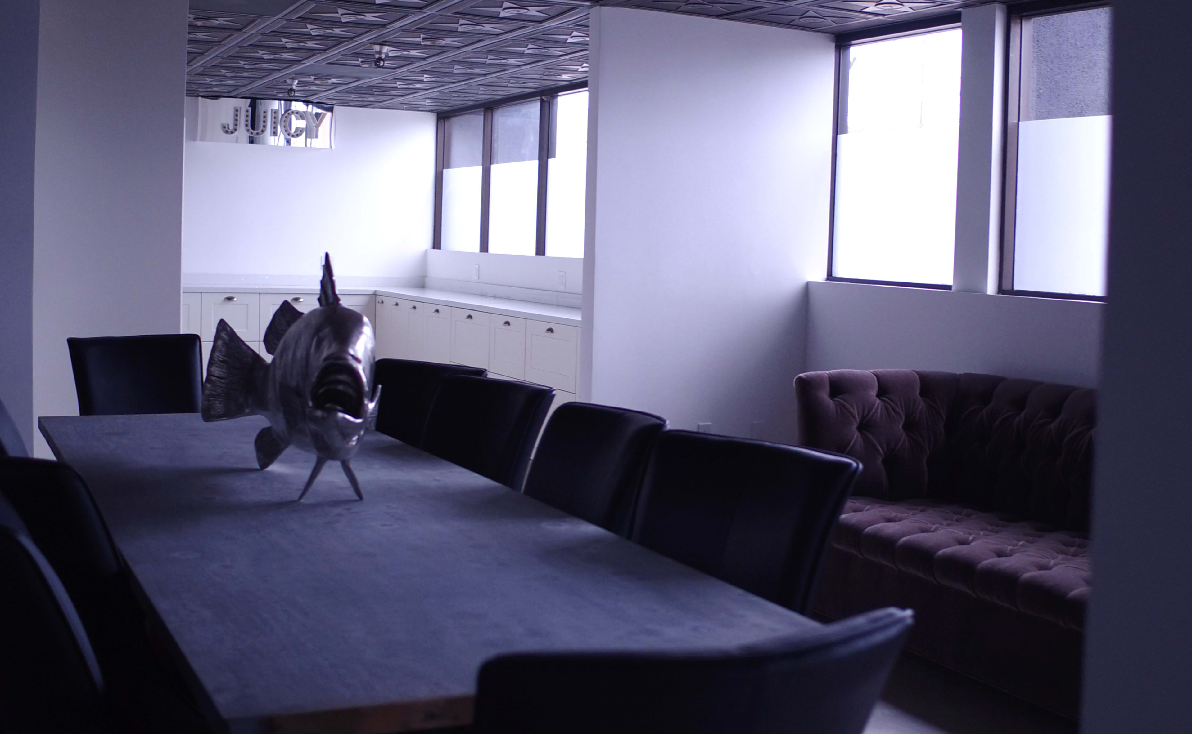 A modern dining area features a large table with a metallic fish sculpture in the center and a tufted sofa against the wall.