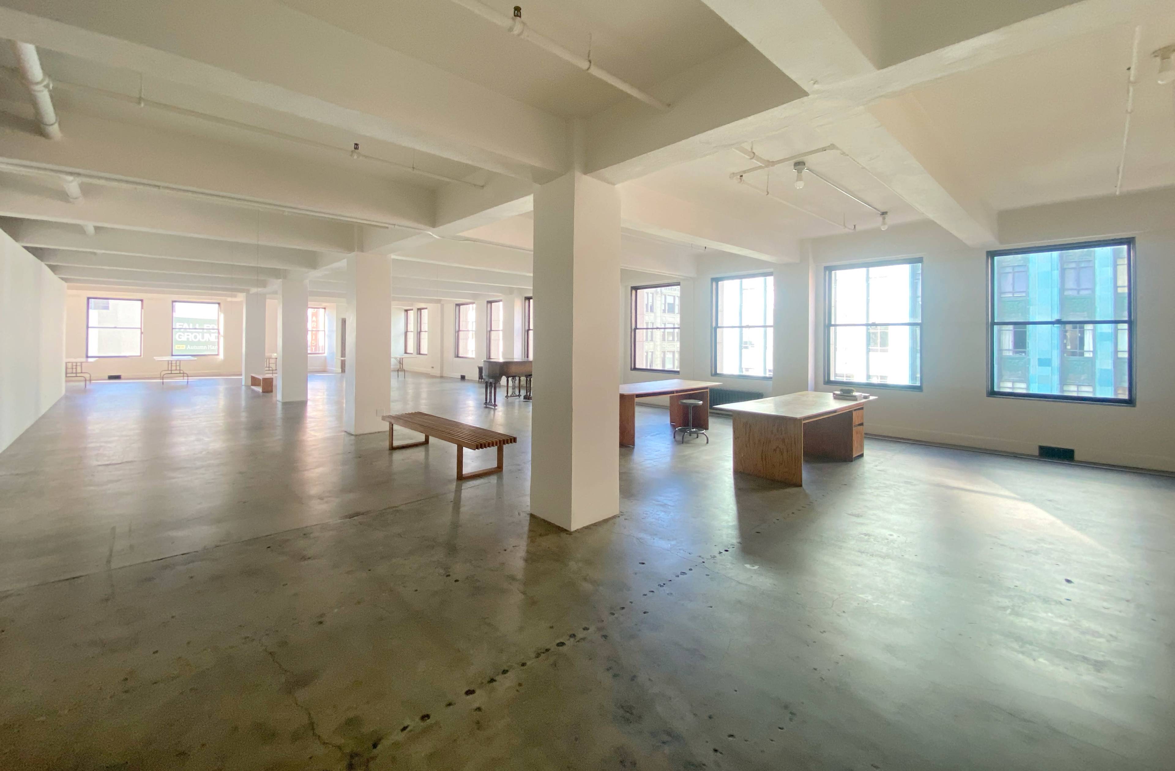 The image shows a spacious, empty office area with large windows and exposed beams.