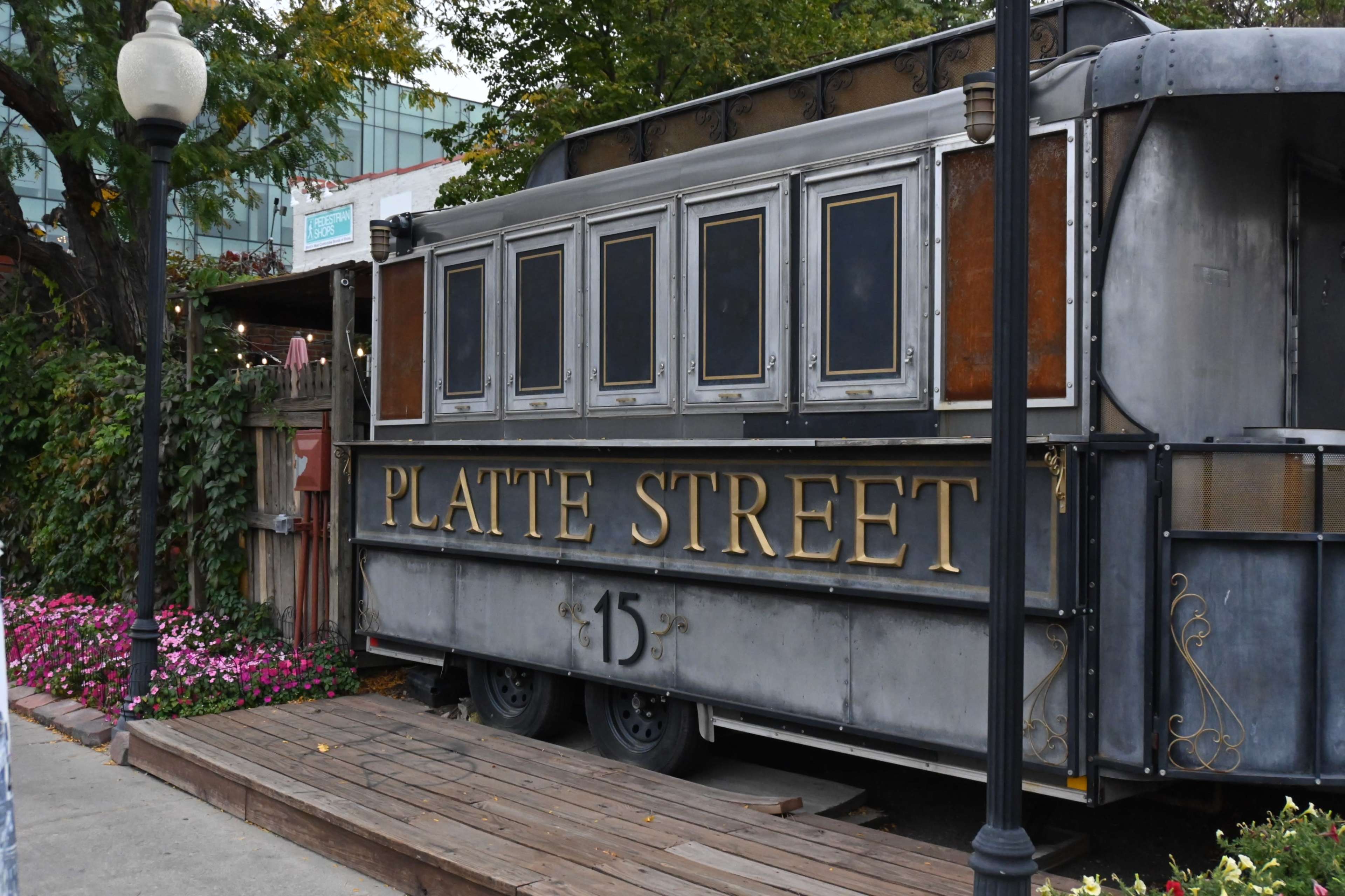 A vintage-style food truck with the name "Platte Street" displayed prominently is parked beside a flowerbed.