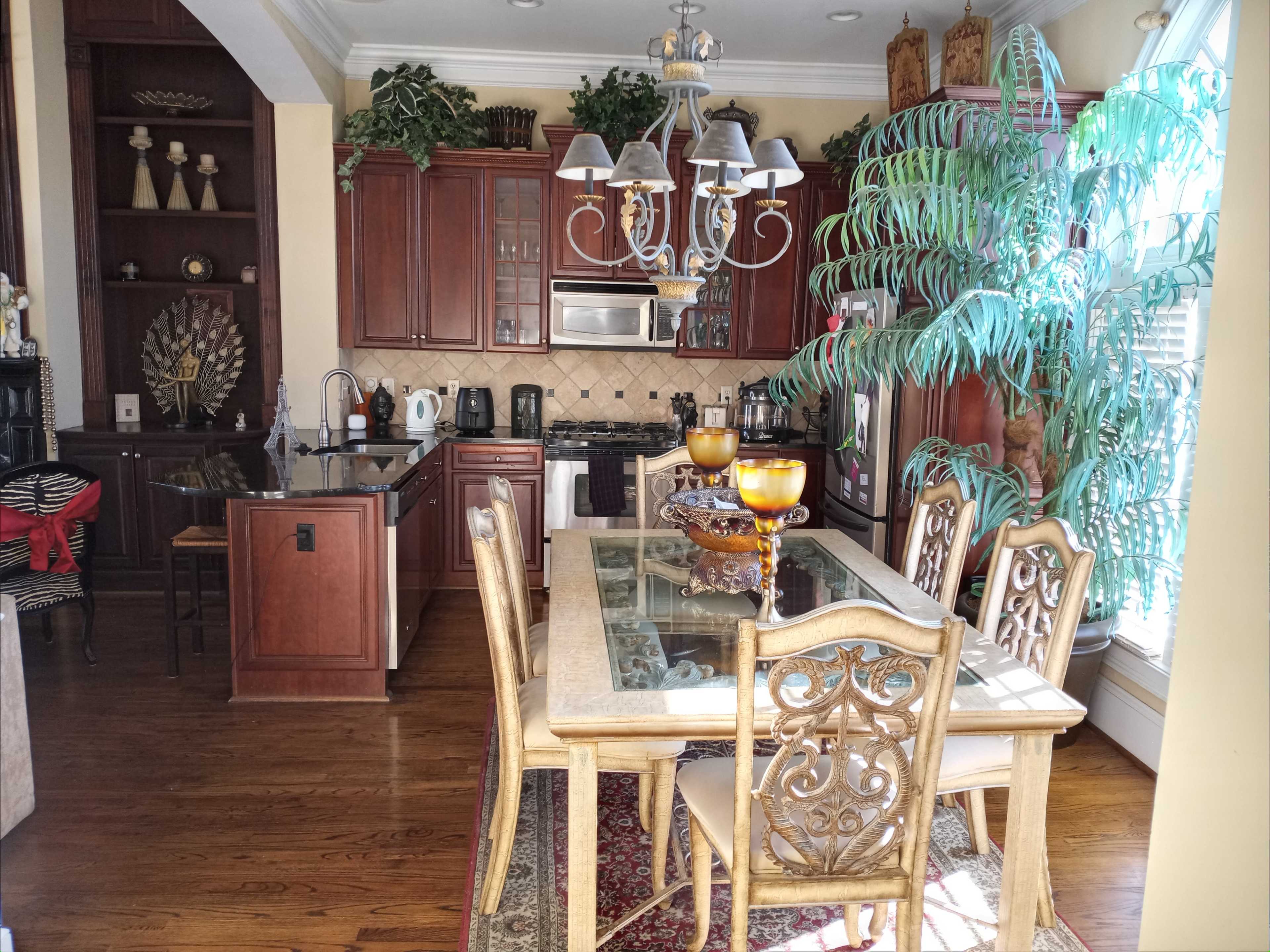 A kitchen and dining area with wooden cabinetry, a chandelier, a dining table, and large plants.