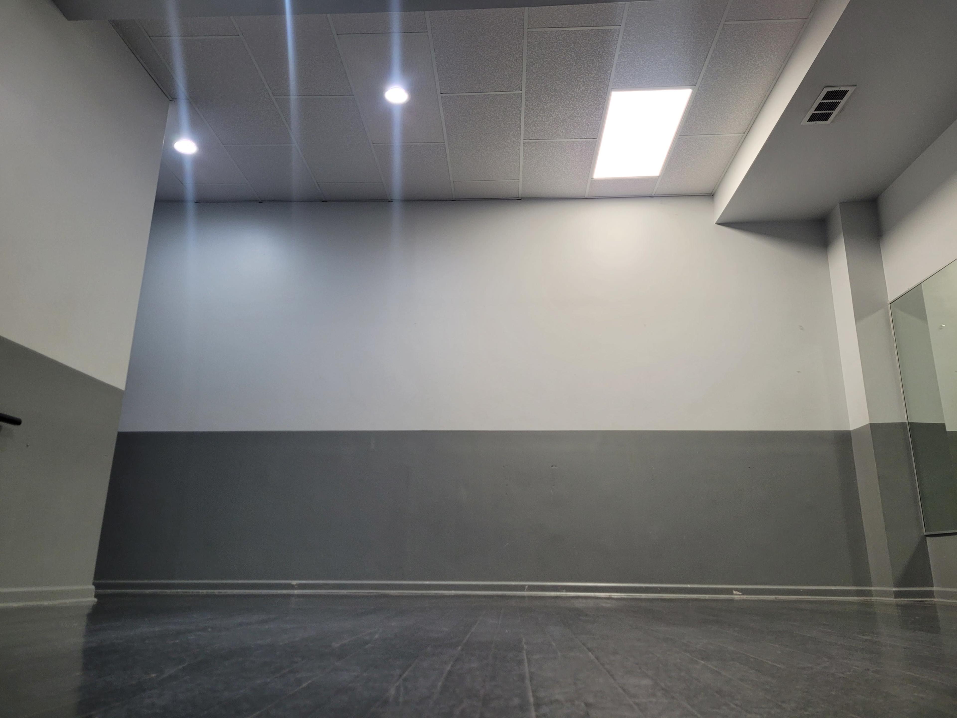 A spacious, minimalist room with a gray and white color scheme, featuring ceiling lights and a large mirror on one wall.