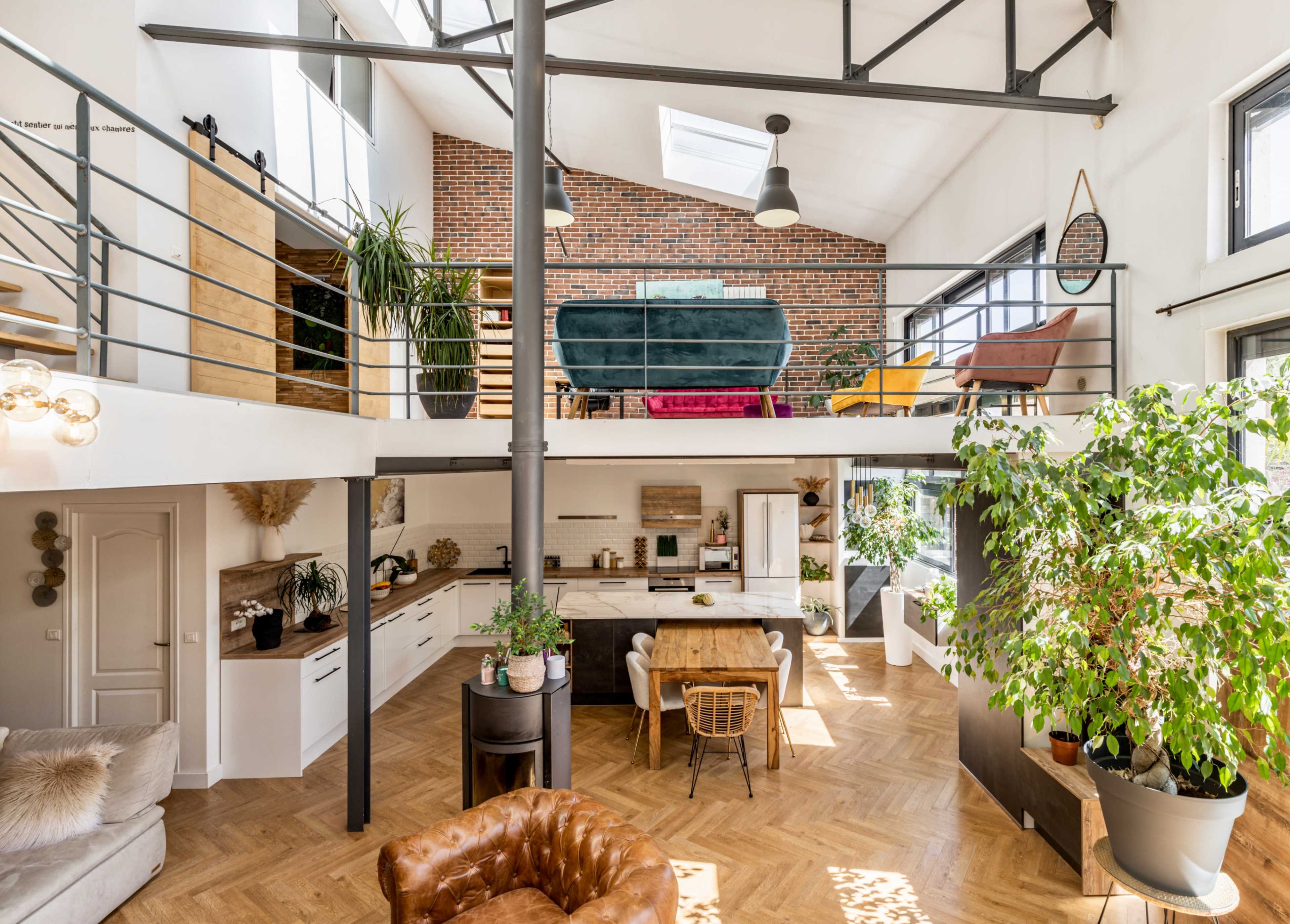 A spacious, modern open-concept living area with a kitchen and dining space, featuring high ceilings, large windows, and greenery throughout.