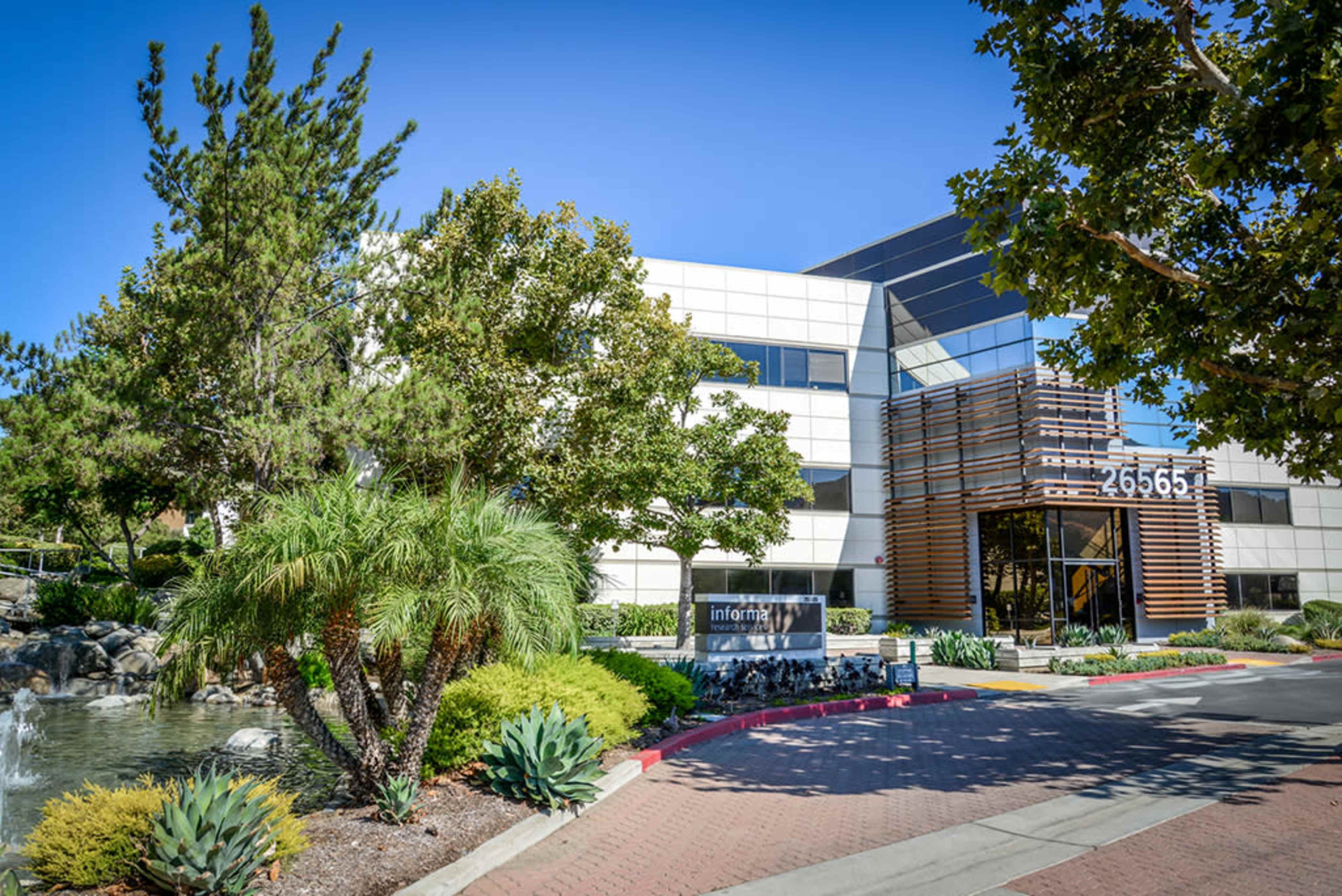 A modern office building surrounded by greenery and a water feature, with a sign indicating the address.