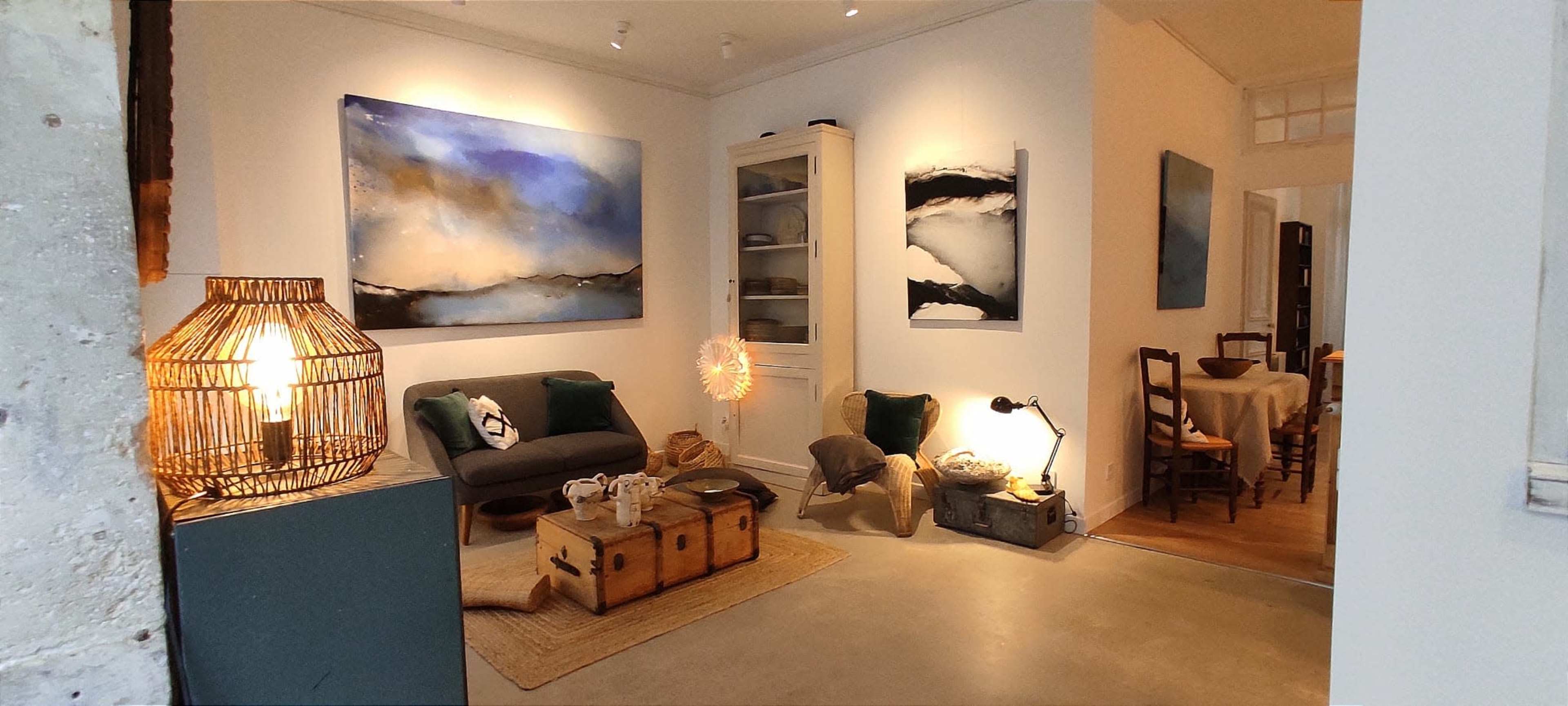 The image shows a cozy living room space featuring a sofa, a coffee table with decorative items, and abstract art on the walls, illuminated by various light sources.