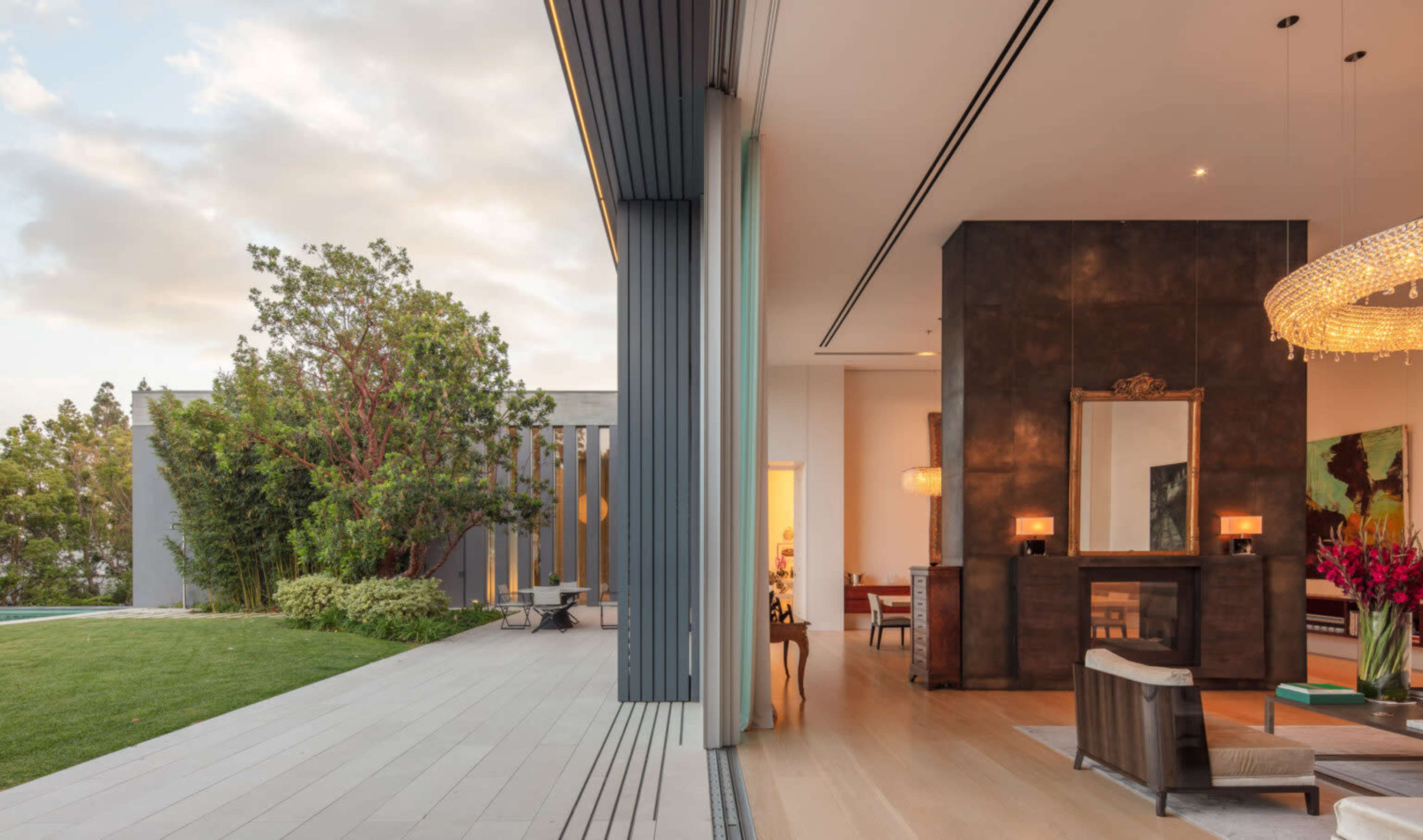 A modern home with an open-concept living area featuring a large mirror and chandelier, seamlessly blending an outdoor patio and landscaped garden.