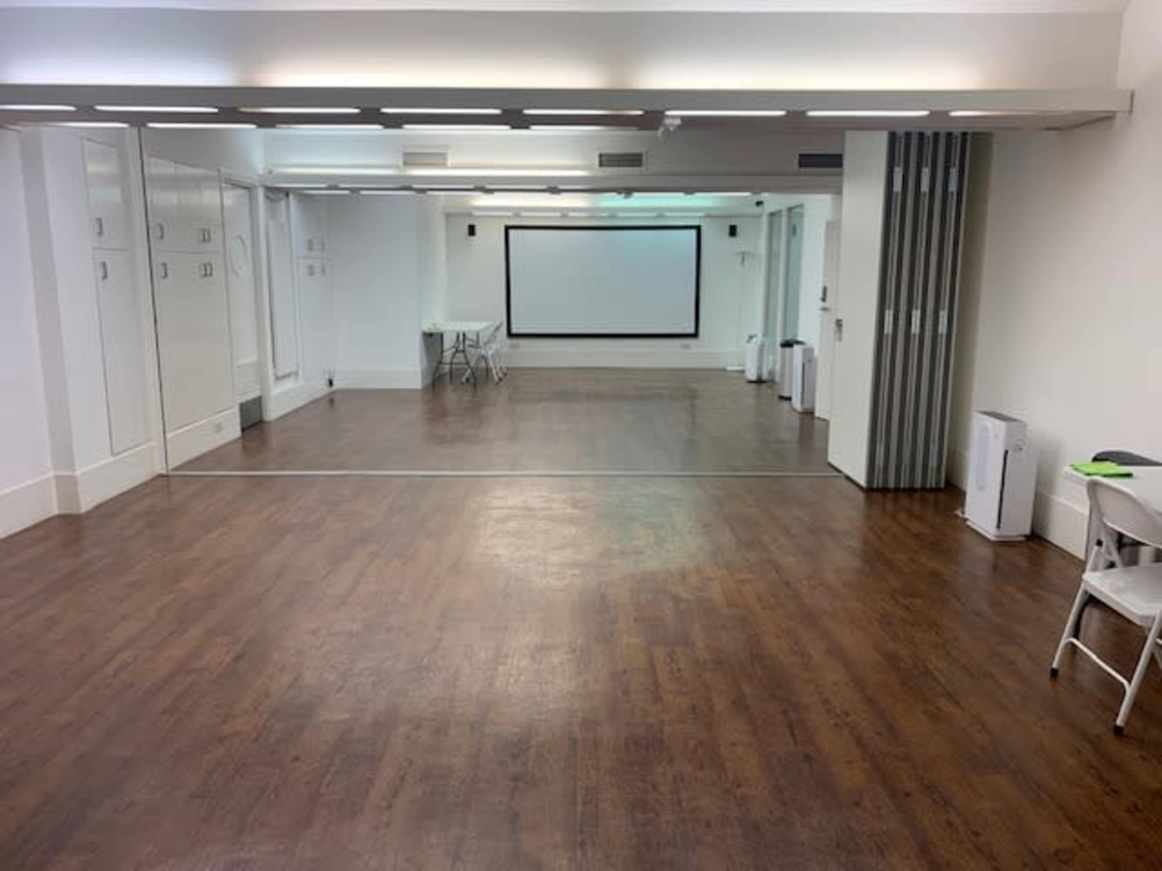 A spacious, empty room with a mirrored wall, a projector screen, and minimal furniture.