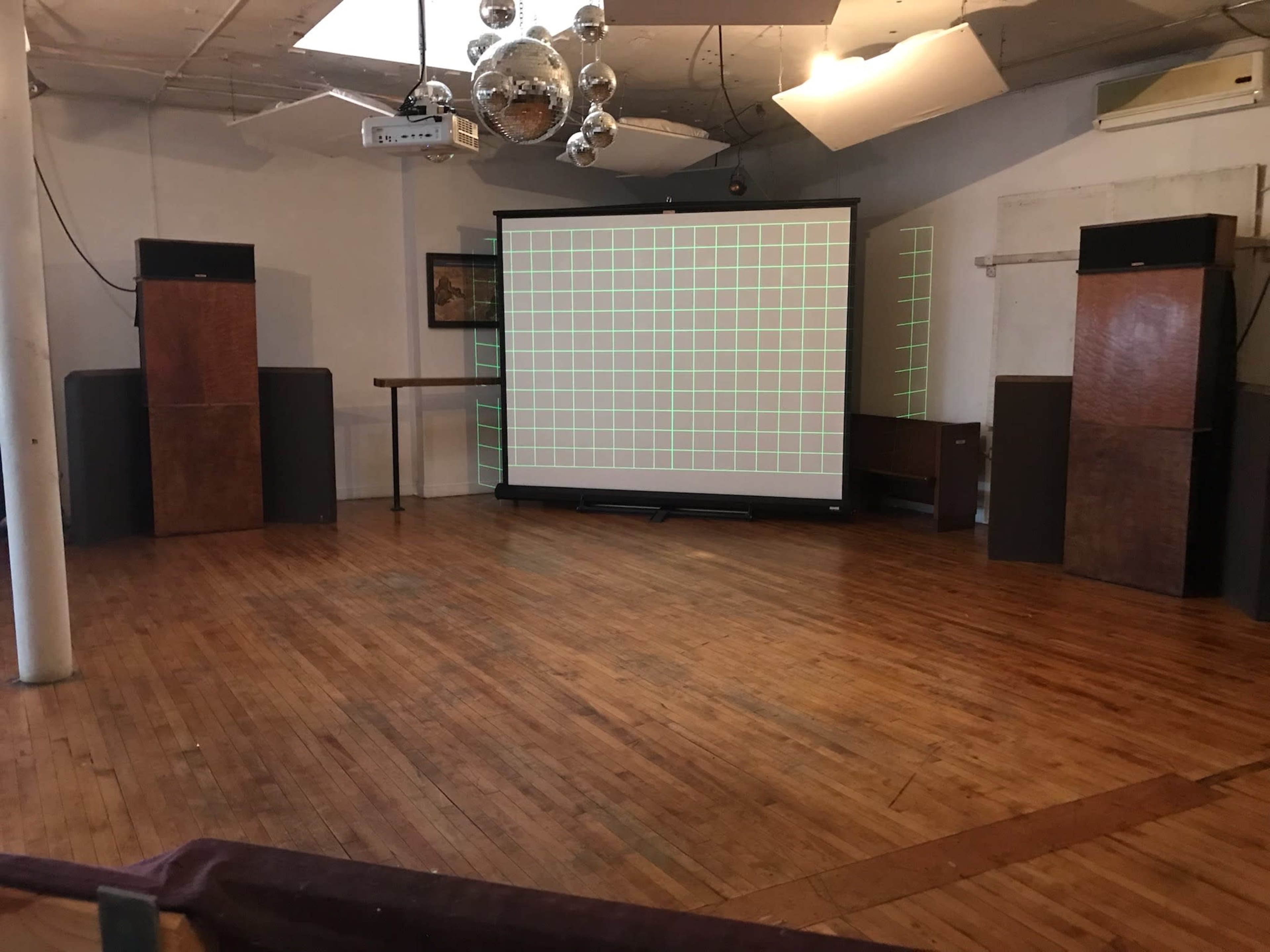 An empty event space featuring a large projection screen with a grid pattern and audio speakers on either side.
