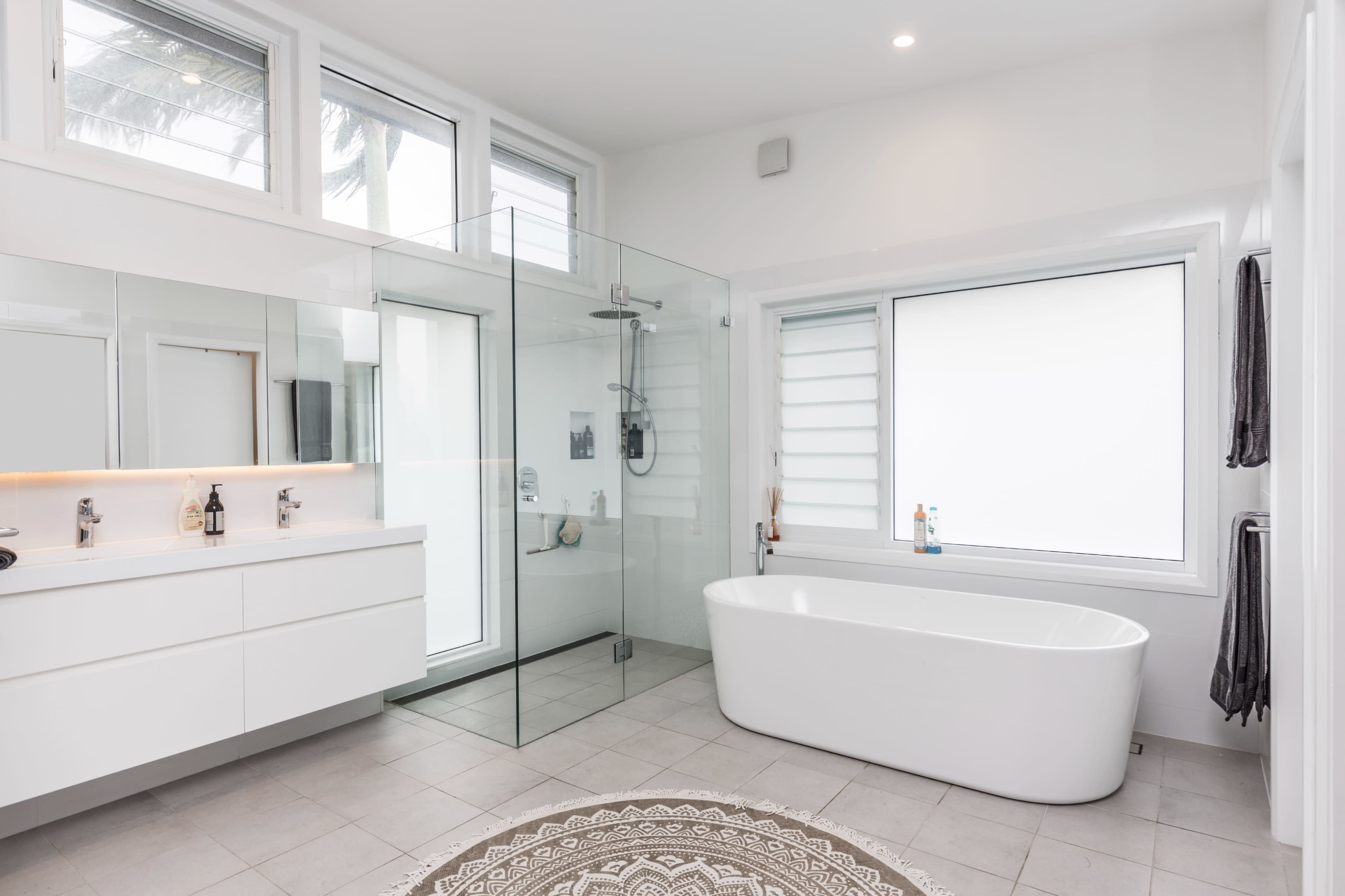 A modern bathroom featuring a glass shower enclosure, a freestanding bathtub, and dual sinks with a large mirror.
