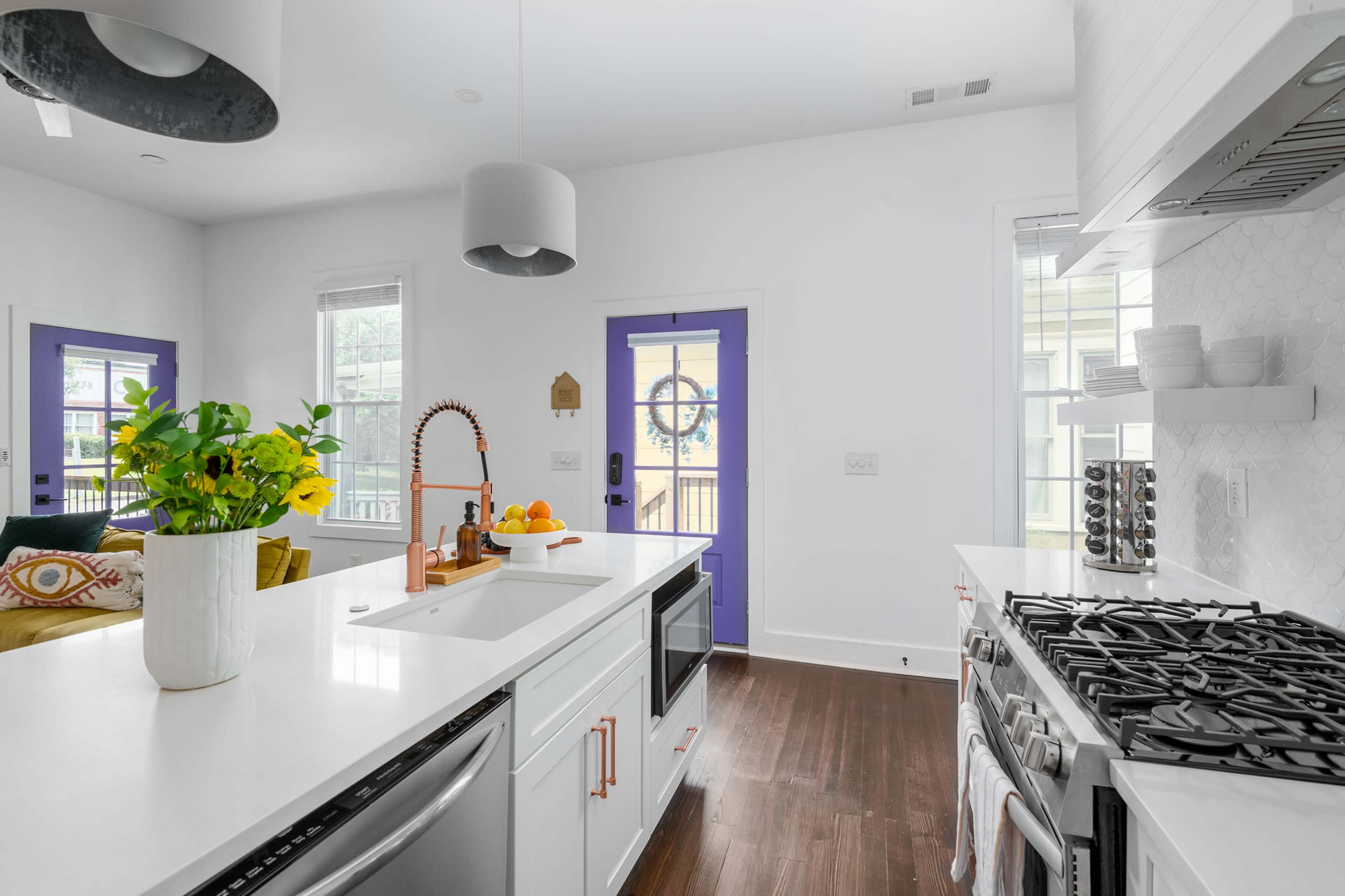 The image shows a modern kitchen with a white countertop, a gas stove, and a bright purple door leading to an outdoor space.