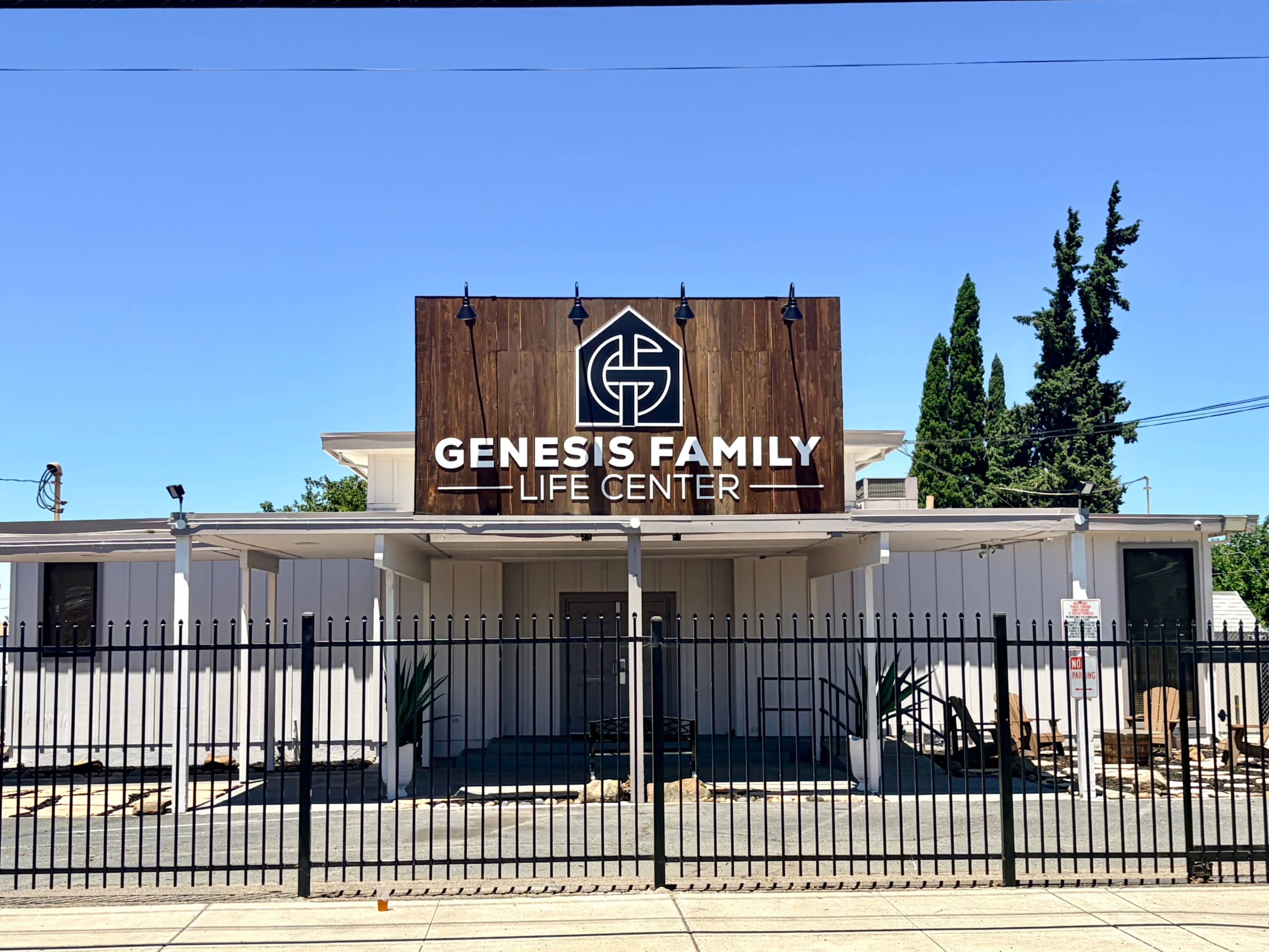The Genesis Family Life Center is a building with a prominent sign featuring its name, surrounded by a black fence and clear blue sky.