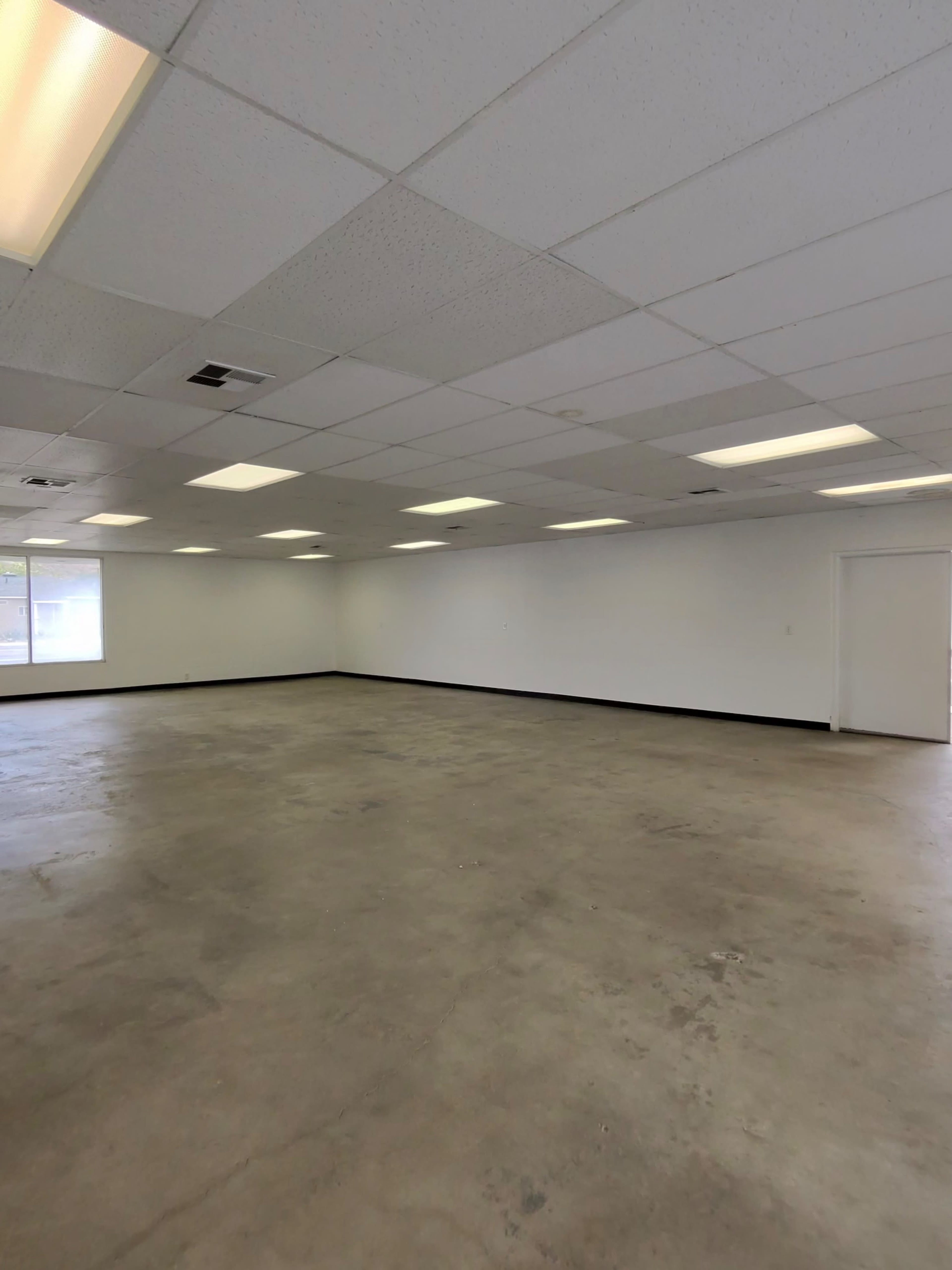 The image shows a large, empty room with concrete flooring and fluorescent lighting.