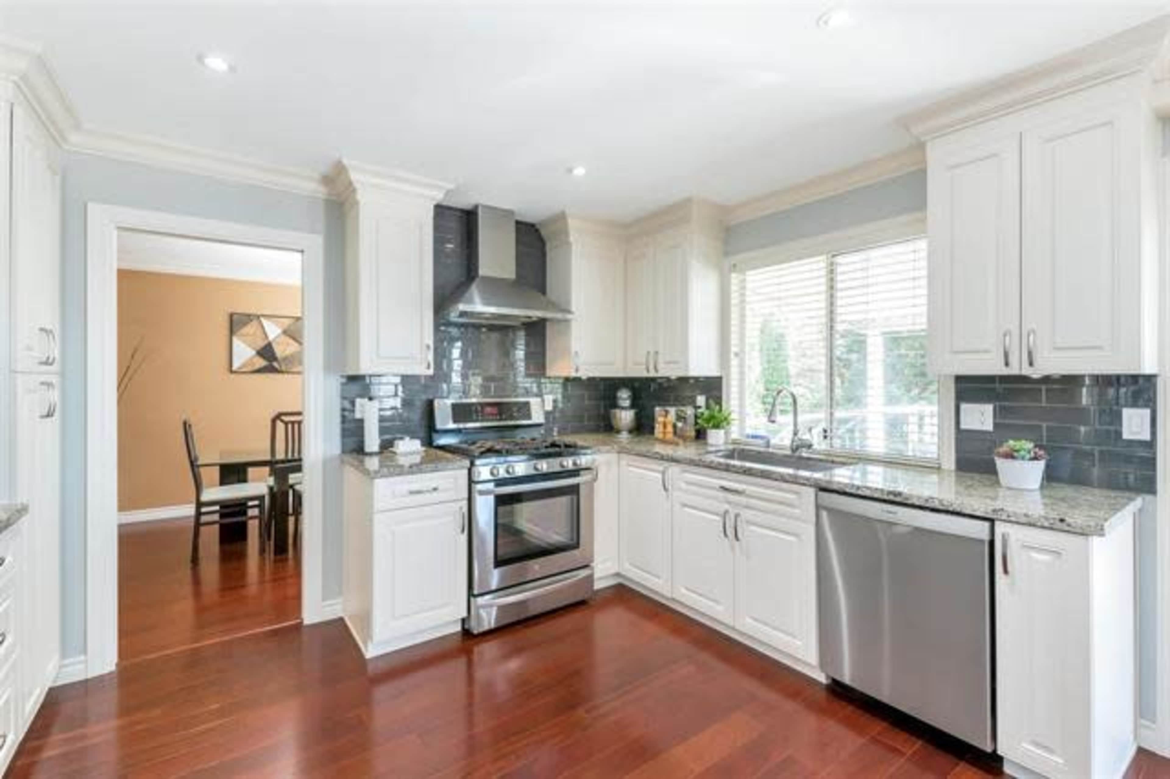 A modern kitchen with white cabinetry, a stainless steel stove and dishwasher, and a window overlooking a dining area.