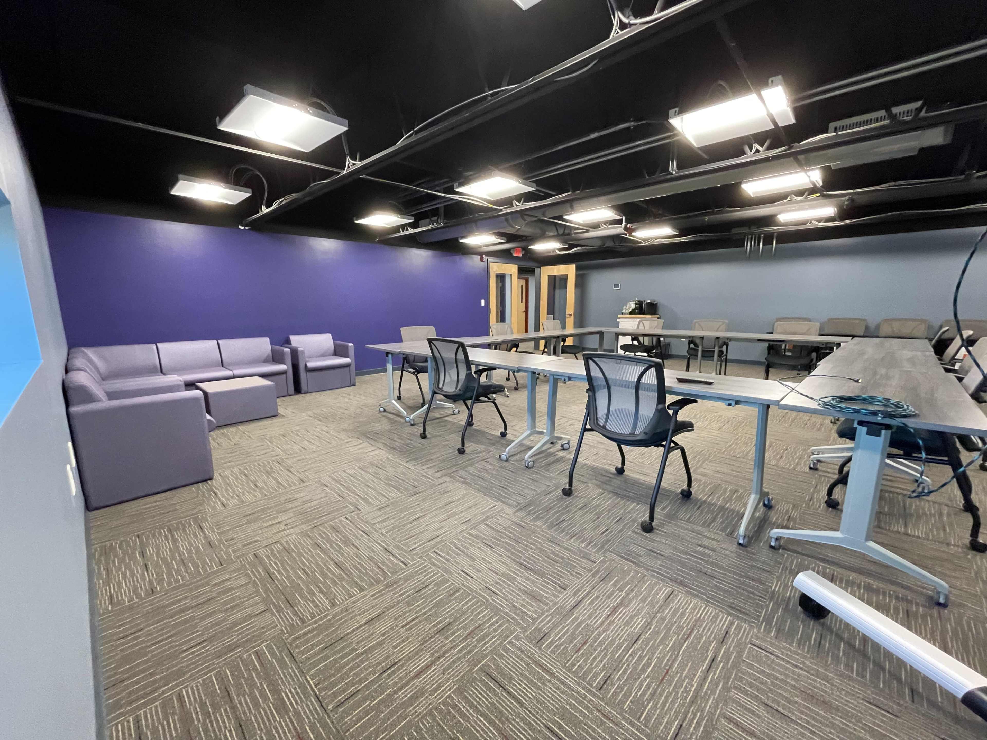 The image shows a meeting room with a large table, several chairs, a couch, and a purple accent wall.