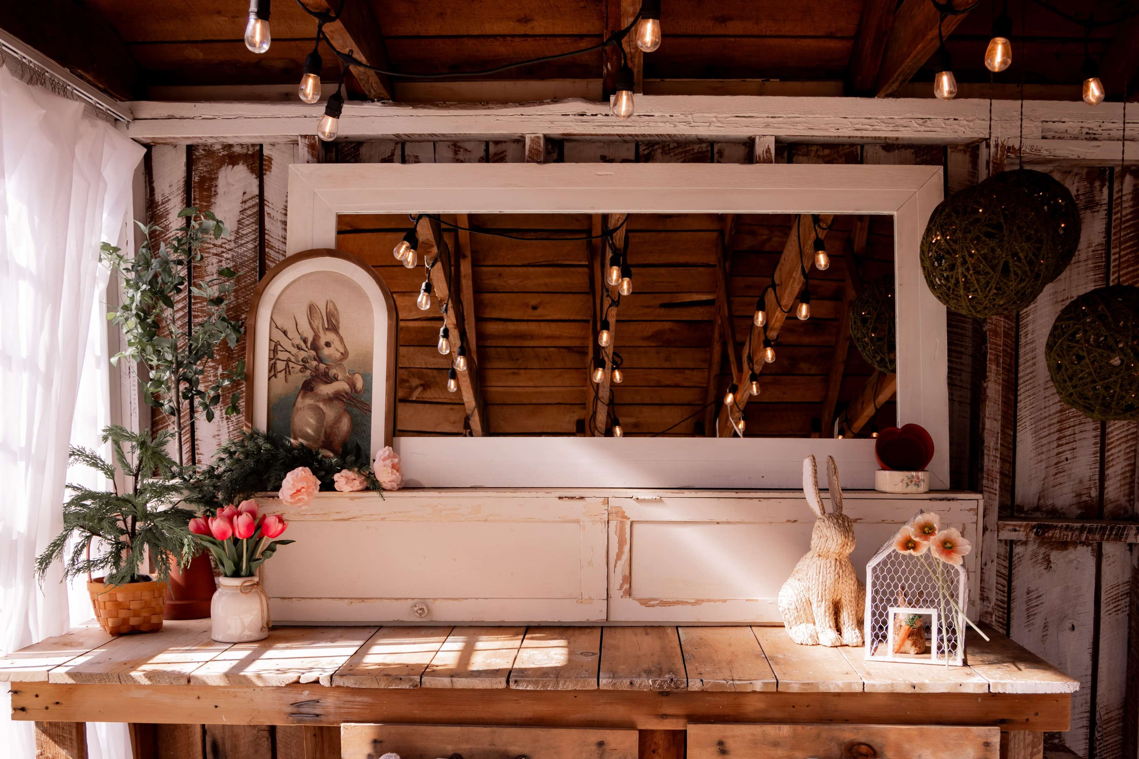 A wooden table adorned with flowers, a vintage mirror, and decorative items, under soft lighting and rustic wooden beams.
