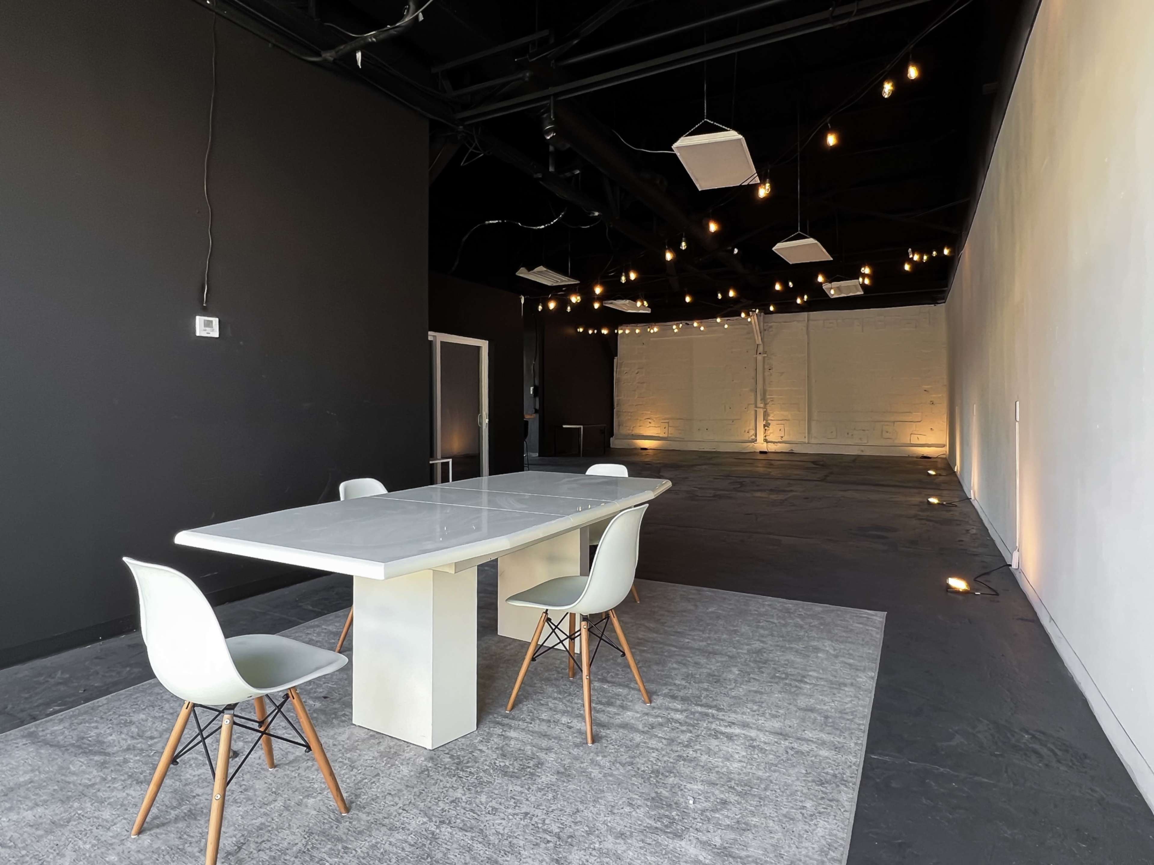 A large, minimalist meeting space features a rectangular table surrounded by four chairs, with soft lighting highlighting the walls.