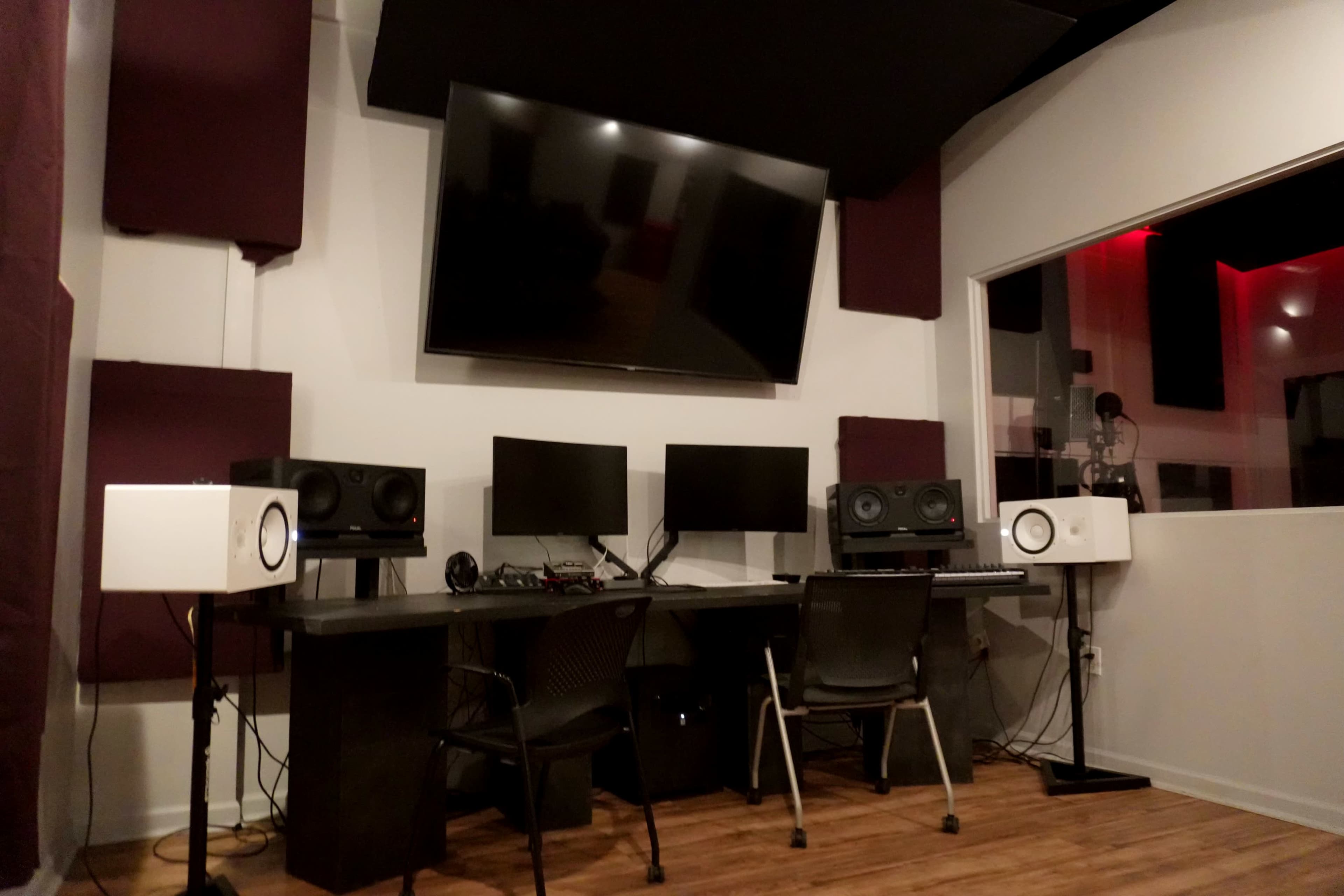 A music production studio featuring a large screen, multiple monitors, studio speakers, and a keyboard arranged around a central workspace.