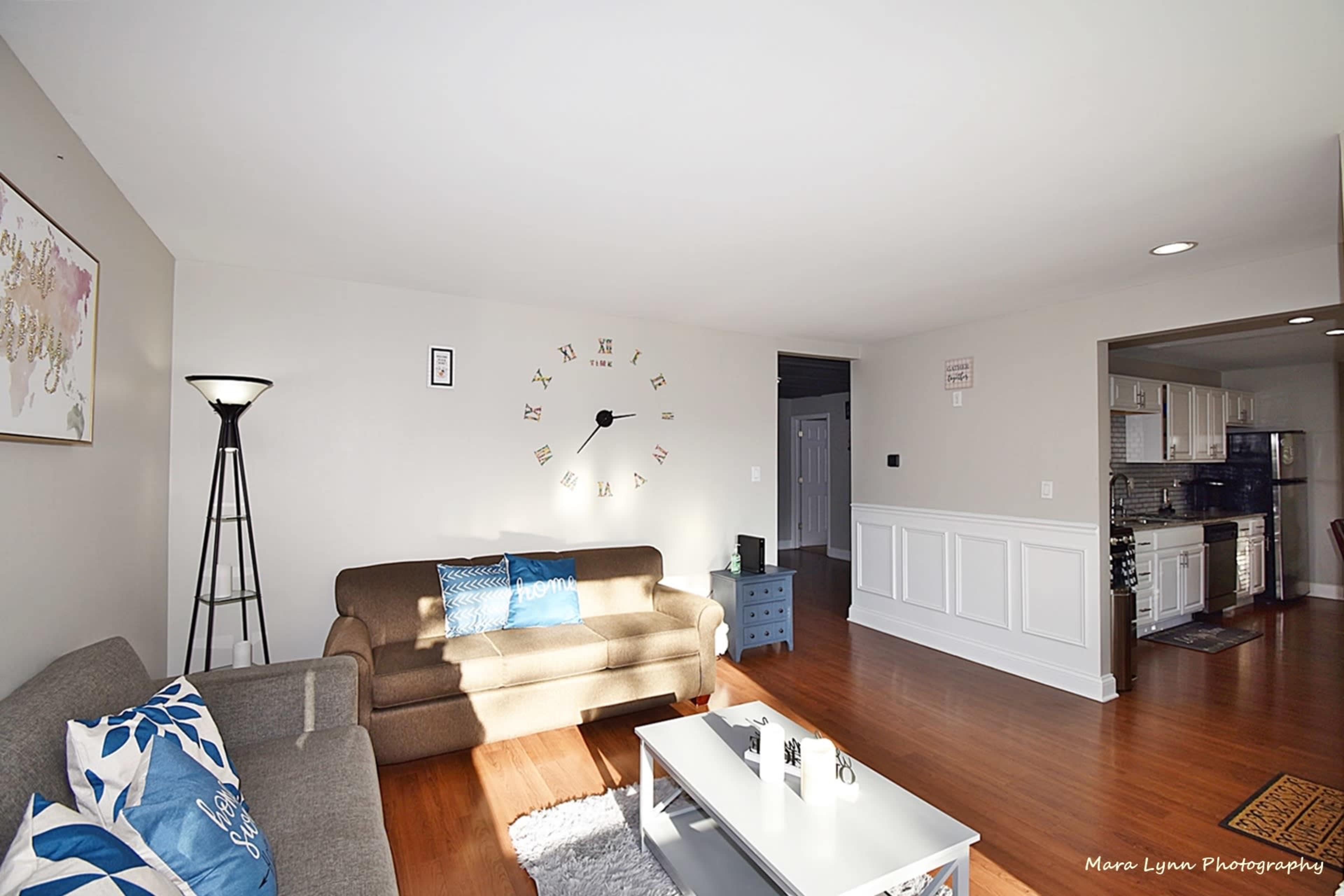 The living room features a sofa, a coffee table, a floor lamp, and a wall clock.