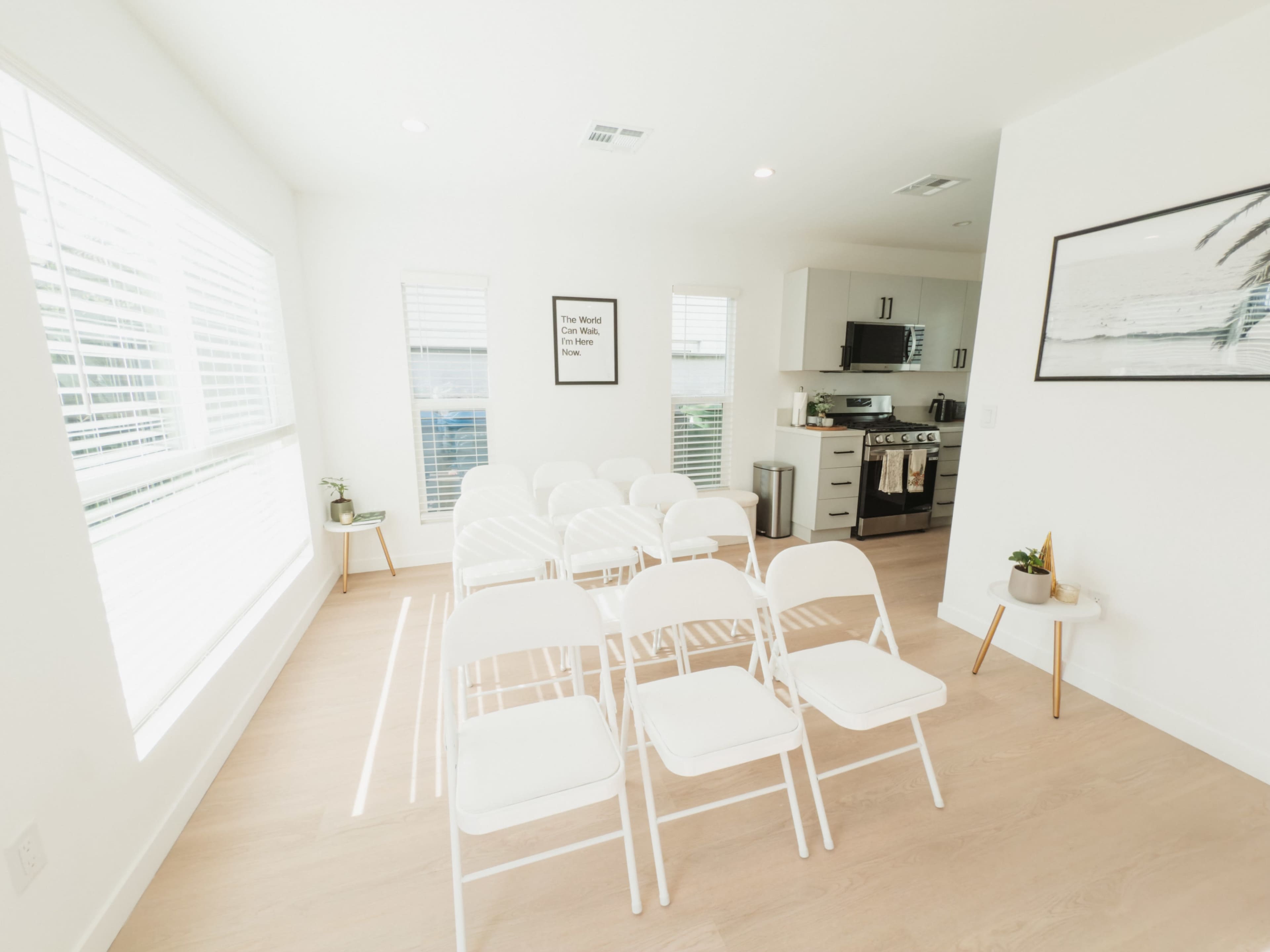 The image shows a clean, bright room with rows of white folding chairs facing a kitchen area in the background.