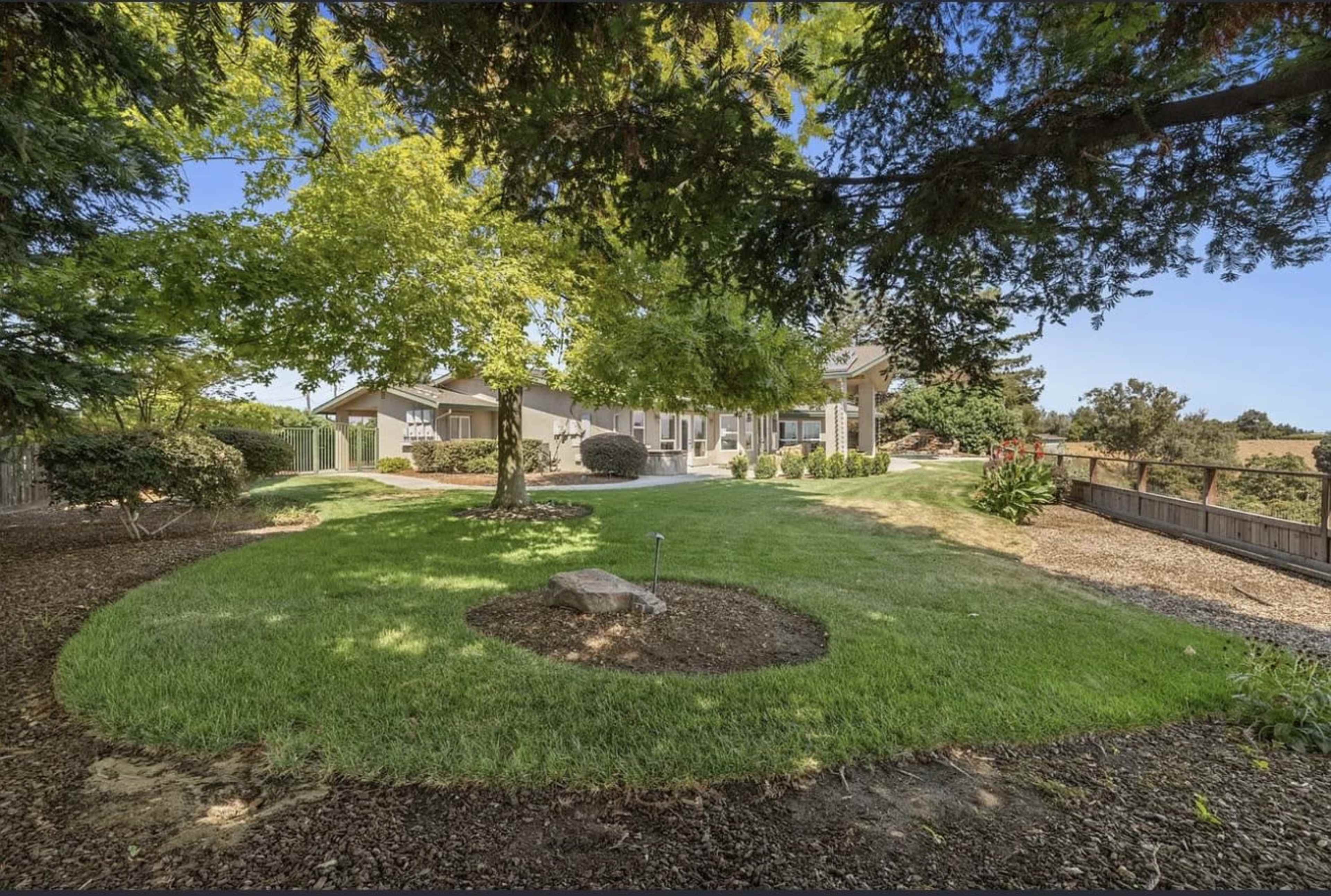 The image shows a lush backyard with a green lawn, surrounded by trees and a house in the background.