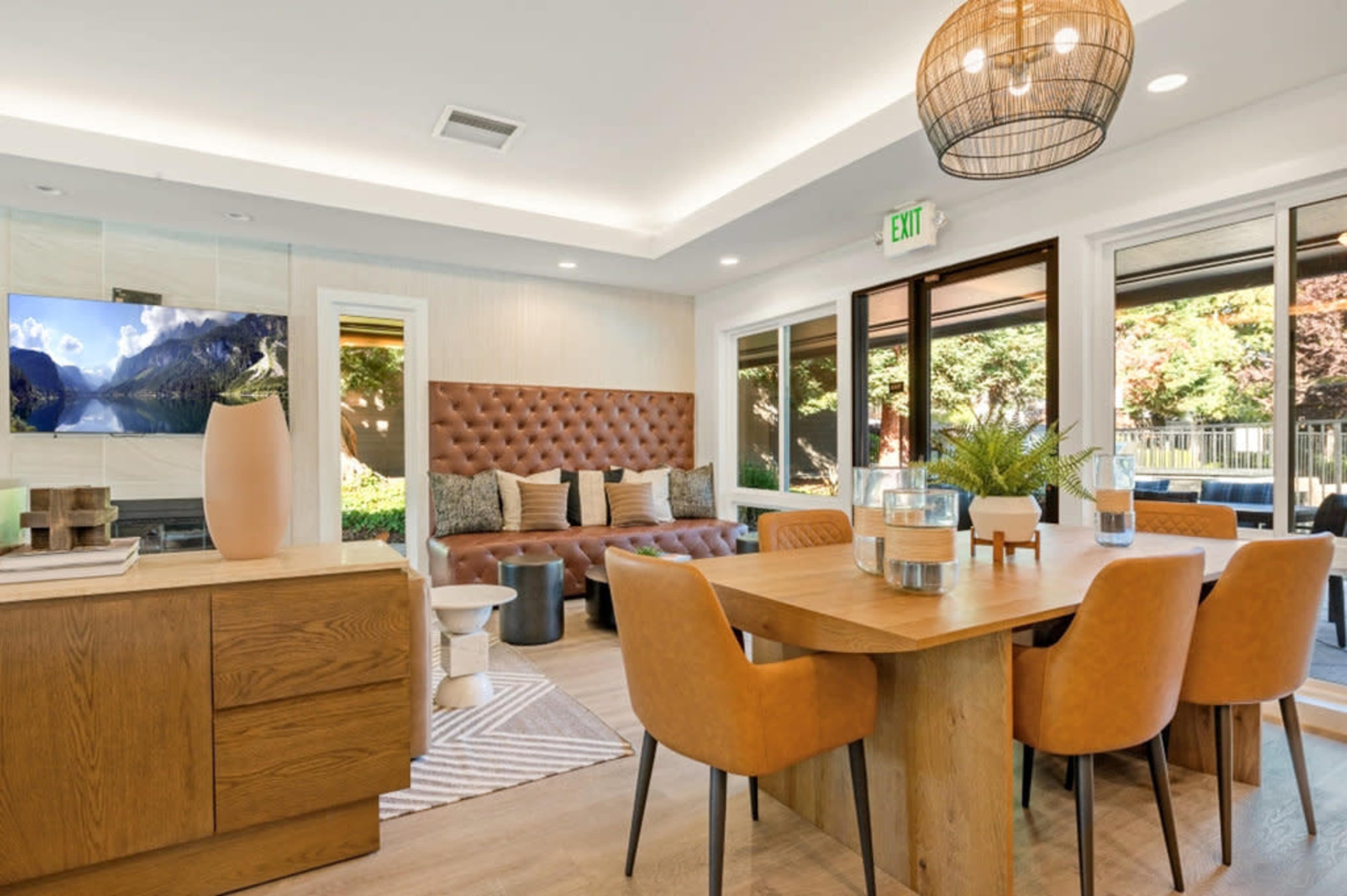 The image shows a stylish dining area with a wooden table surrounded by leather chairs, a modern sideboard, and a large window that offers a view of an outdoor space.