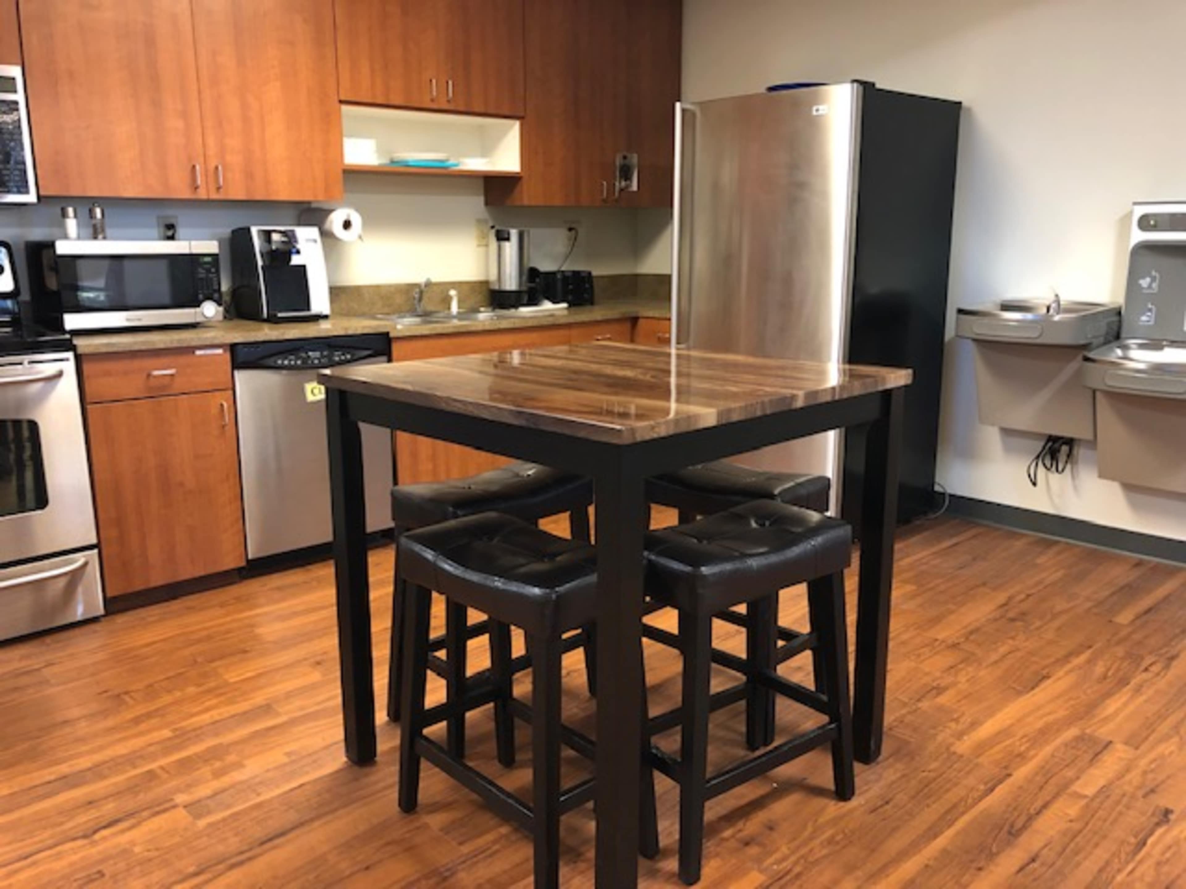 A kitchen area with wooden cabinets, stainless steel appliances, a tall table, and four black stools.