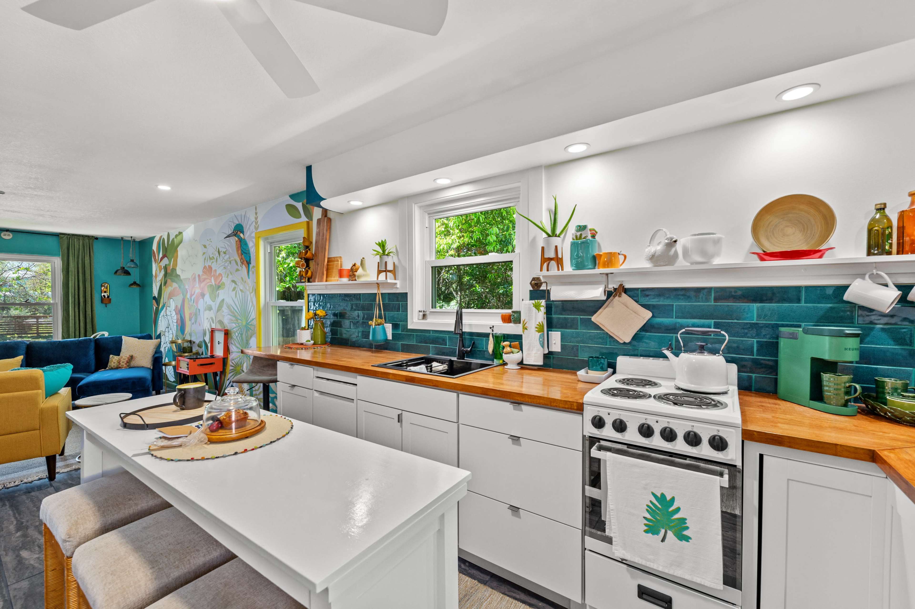 A bright kitchen features white cabinetry, a wooden countertop, a vintage stove, and shelves adorned with plants and decorative items.