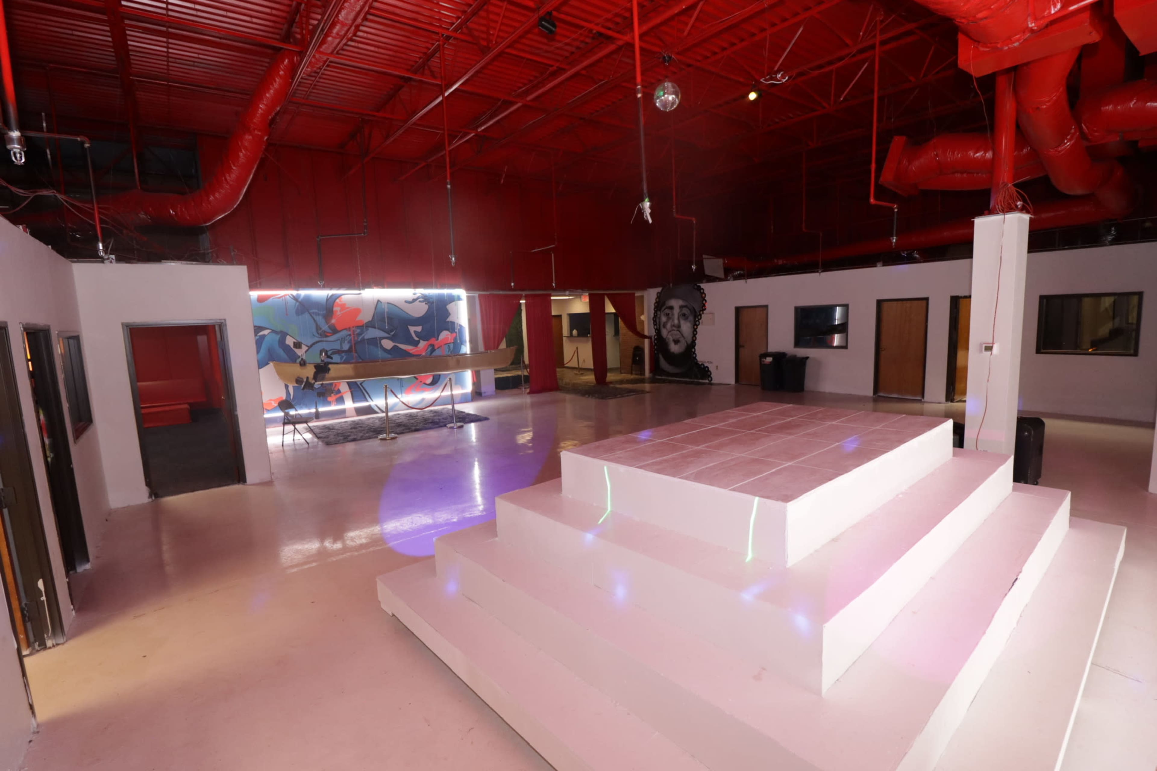 A spacious interior with a raised white platform, red walls, and a colorful mural on one side.