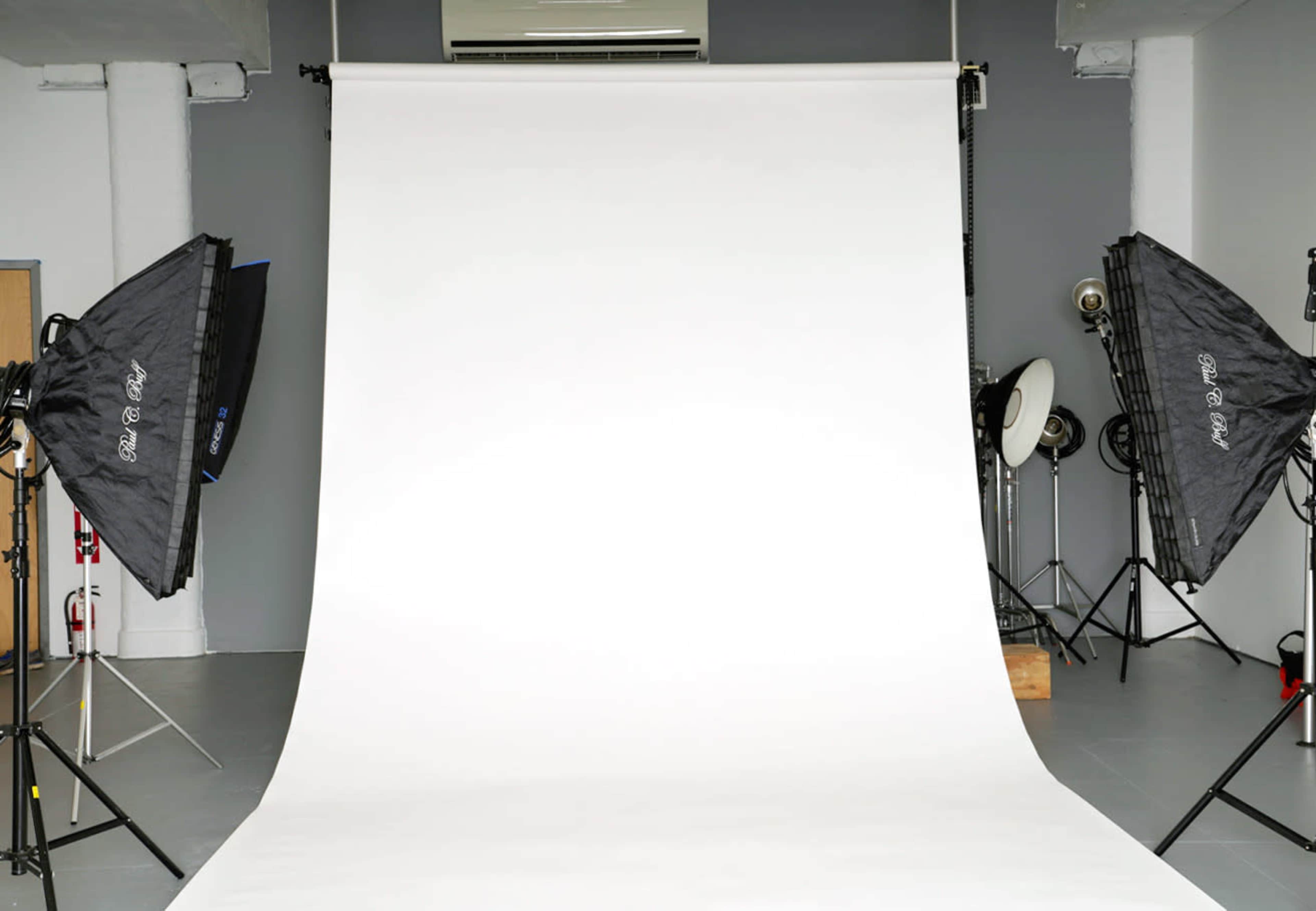 A photography studio features a white backdrop with two softbox lights positioned on either side.