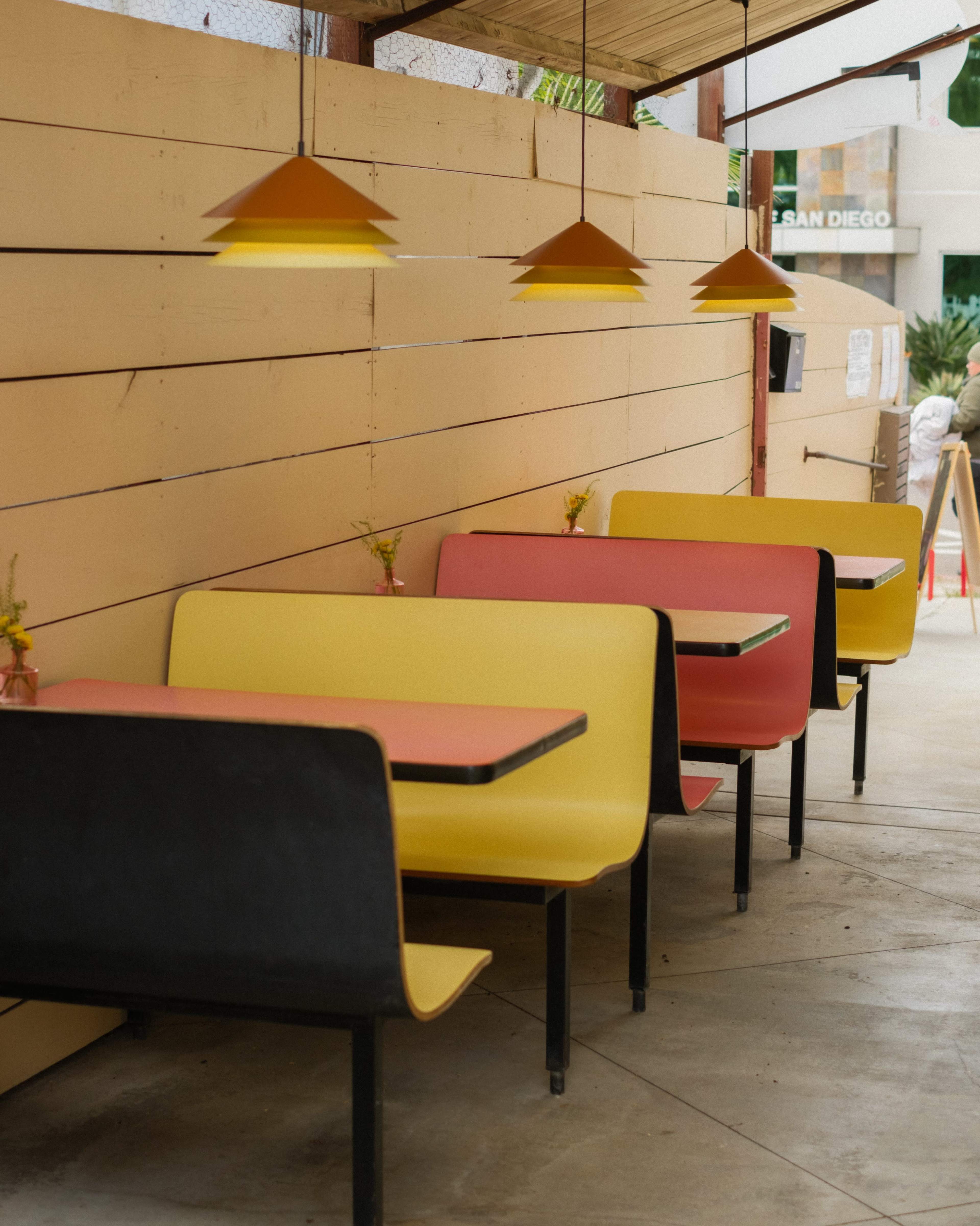 The image shows a row of brightly colored yellow and red booth seats arranged along a wooden wall in a casual dining area.