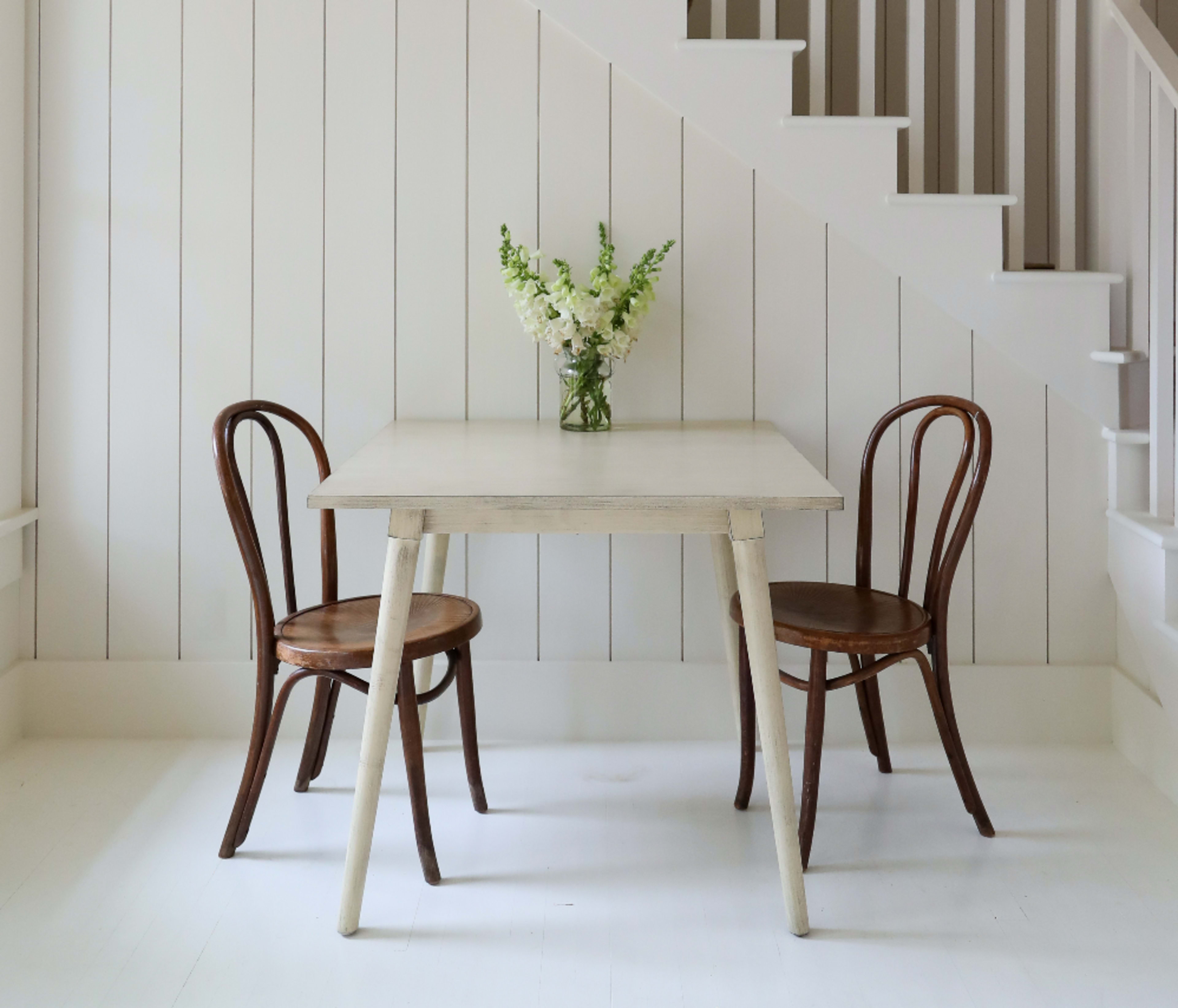 A small table with two chairs and a vase of flowers is situated next to a staircase with wooden steps.