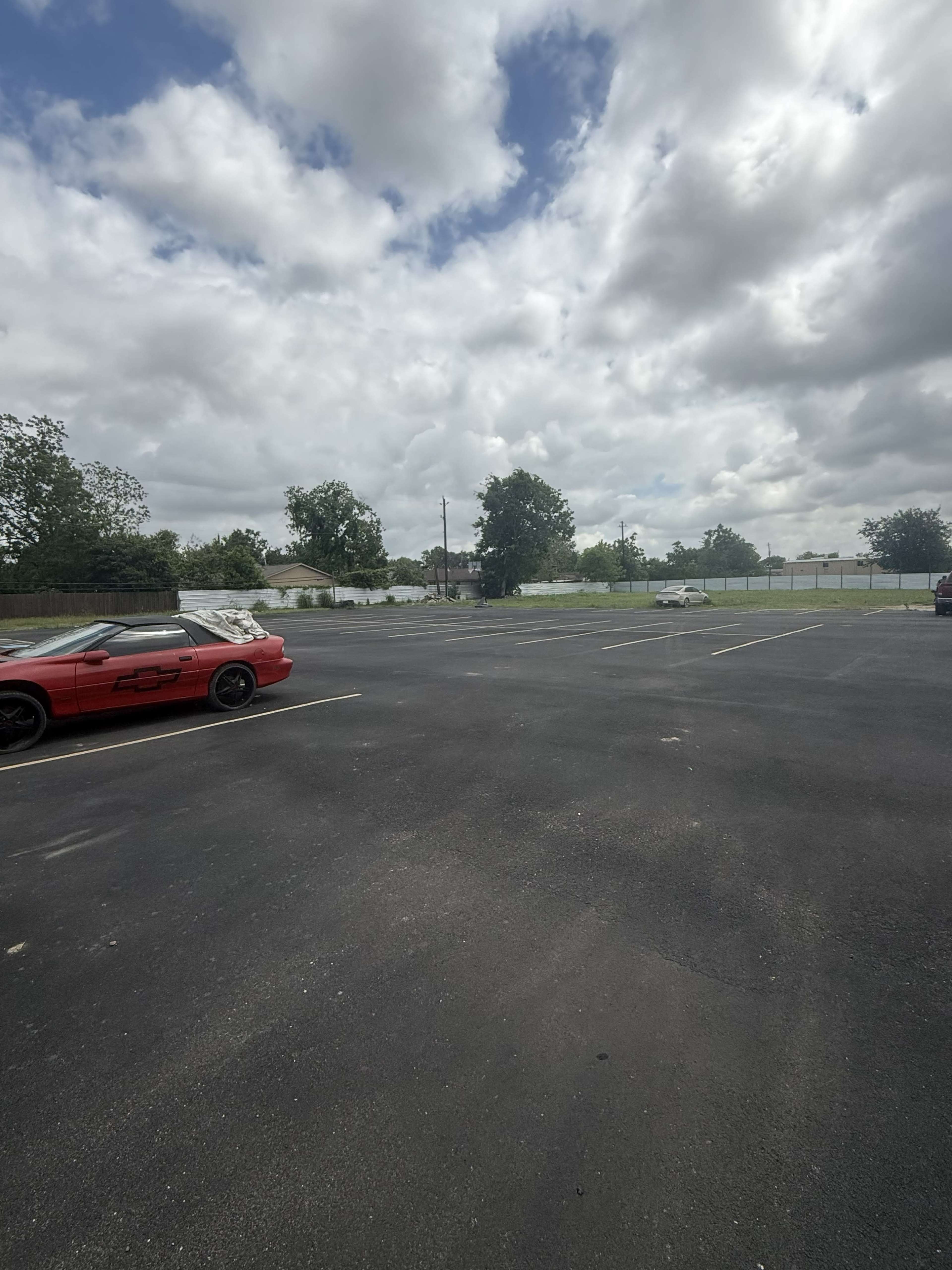 An empty parking lot features a few scattered cars beneath a cloudy sky.