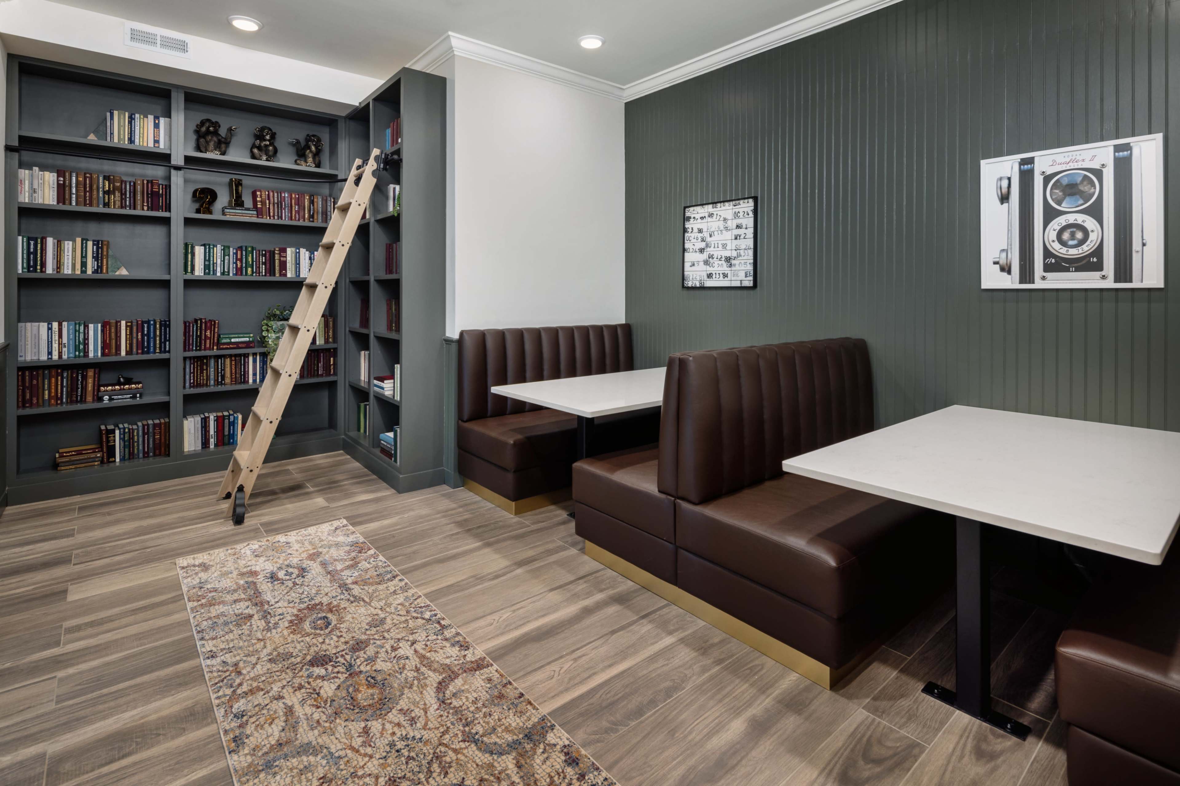 A cozy reading nook with two brown leather banquettes, a bookshelf filled with books, and a wooden ladder leaning against the shelves.