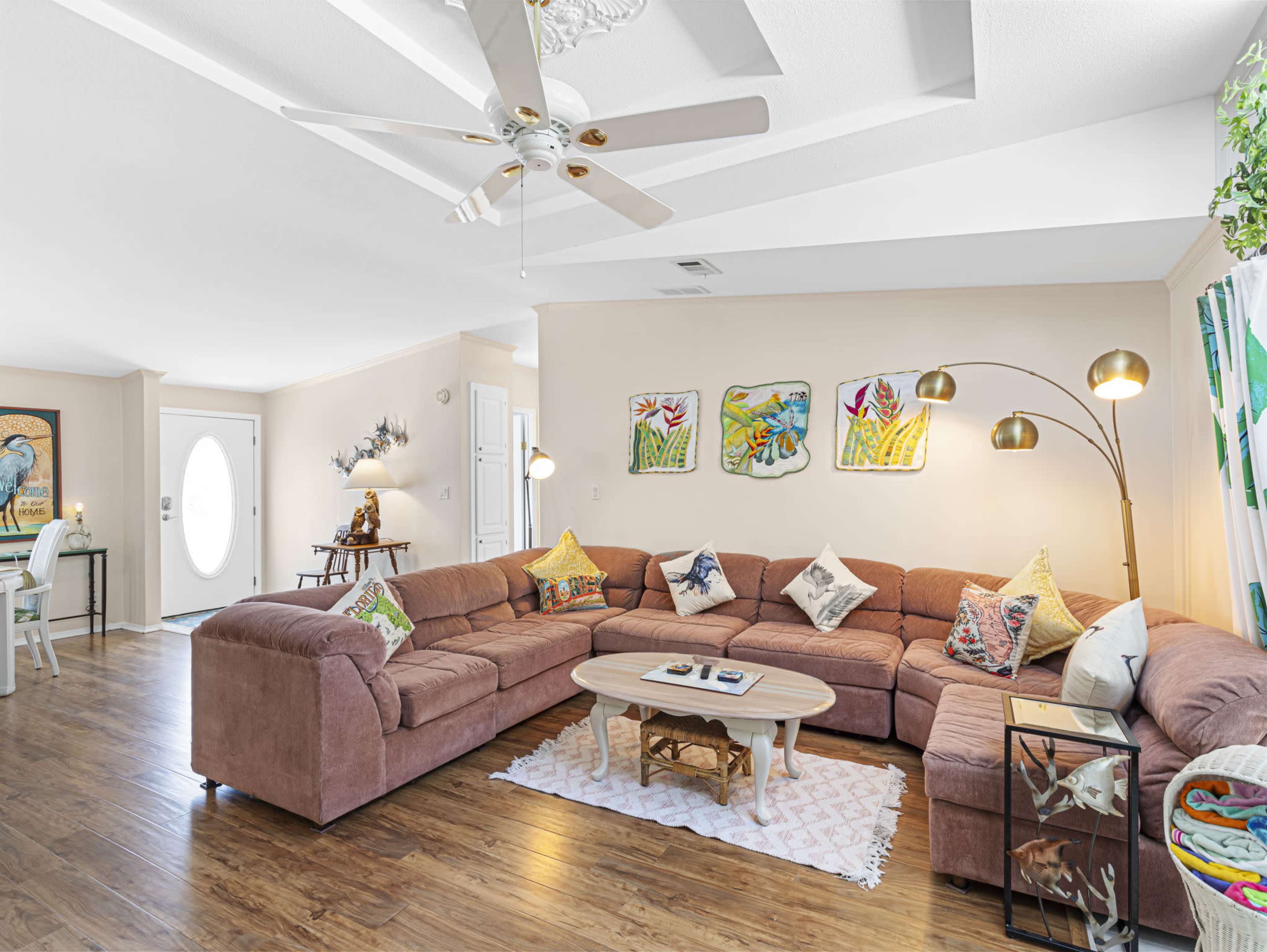 A spacious living room features a large, L-shaped sofa, a round coffee table, and colorful artwork on the walls.