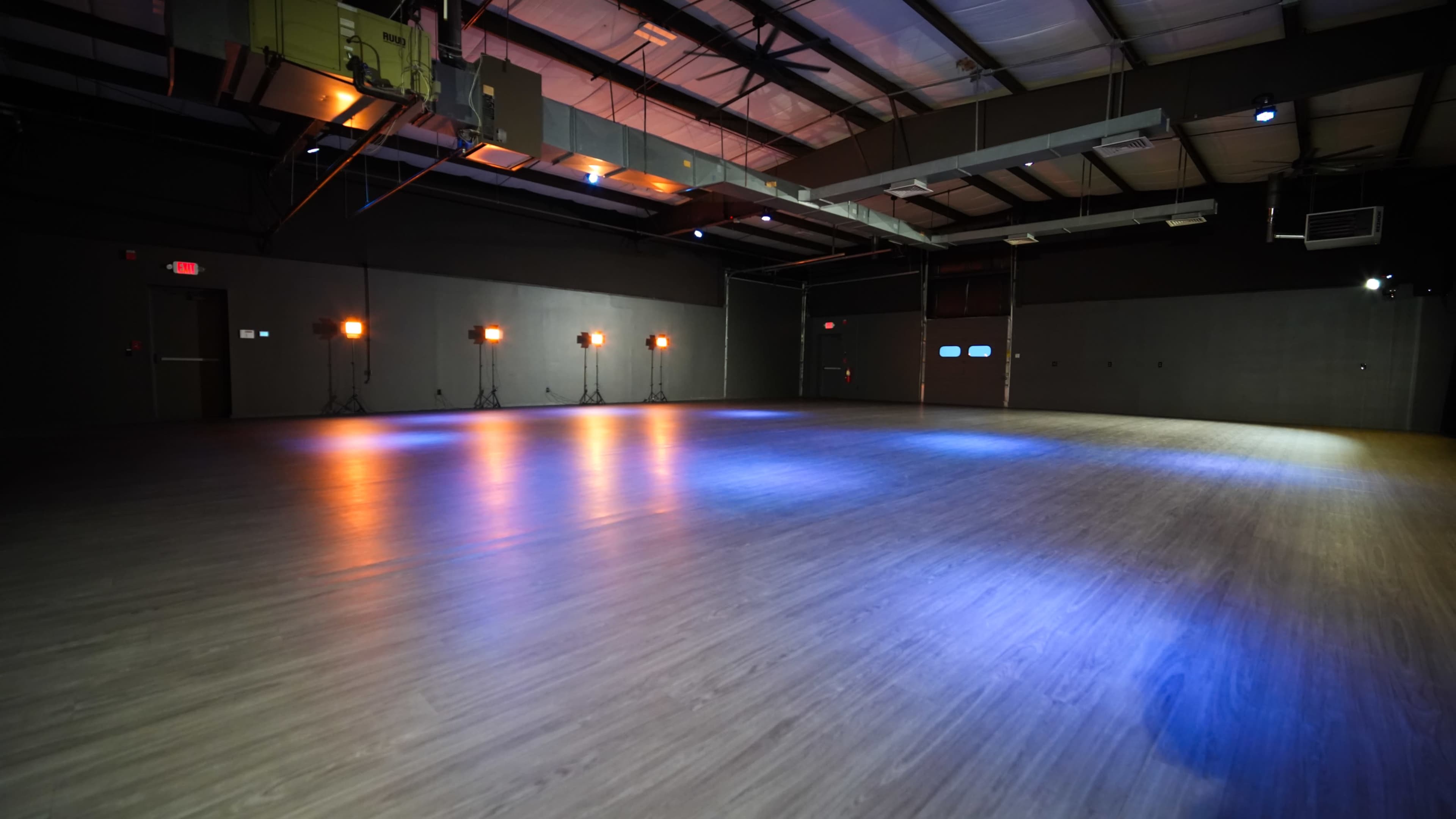 The image shows a spacious, illuminated indoor venue with a polished wooden floor and spotlights arranged around the perimeter.