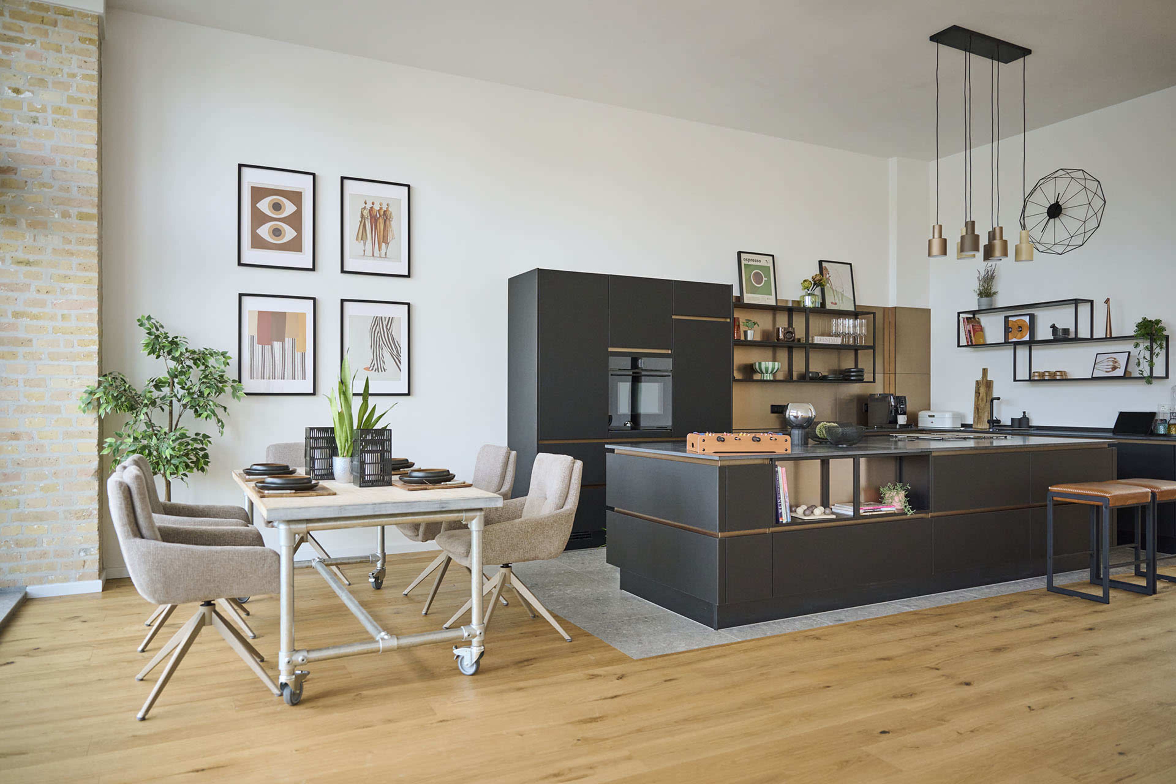 A modern kitchen features a black cabinetry setup, a dining table with beige chairs, and framed artwork on the walls.