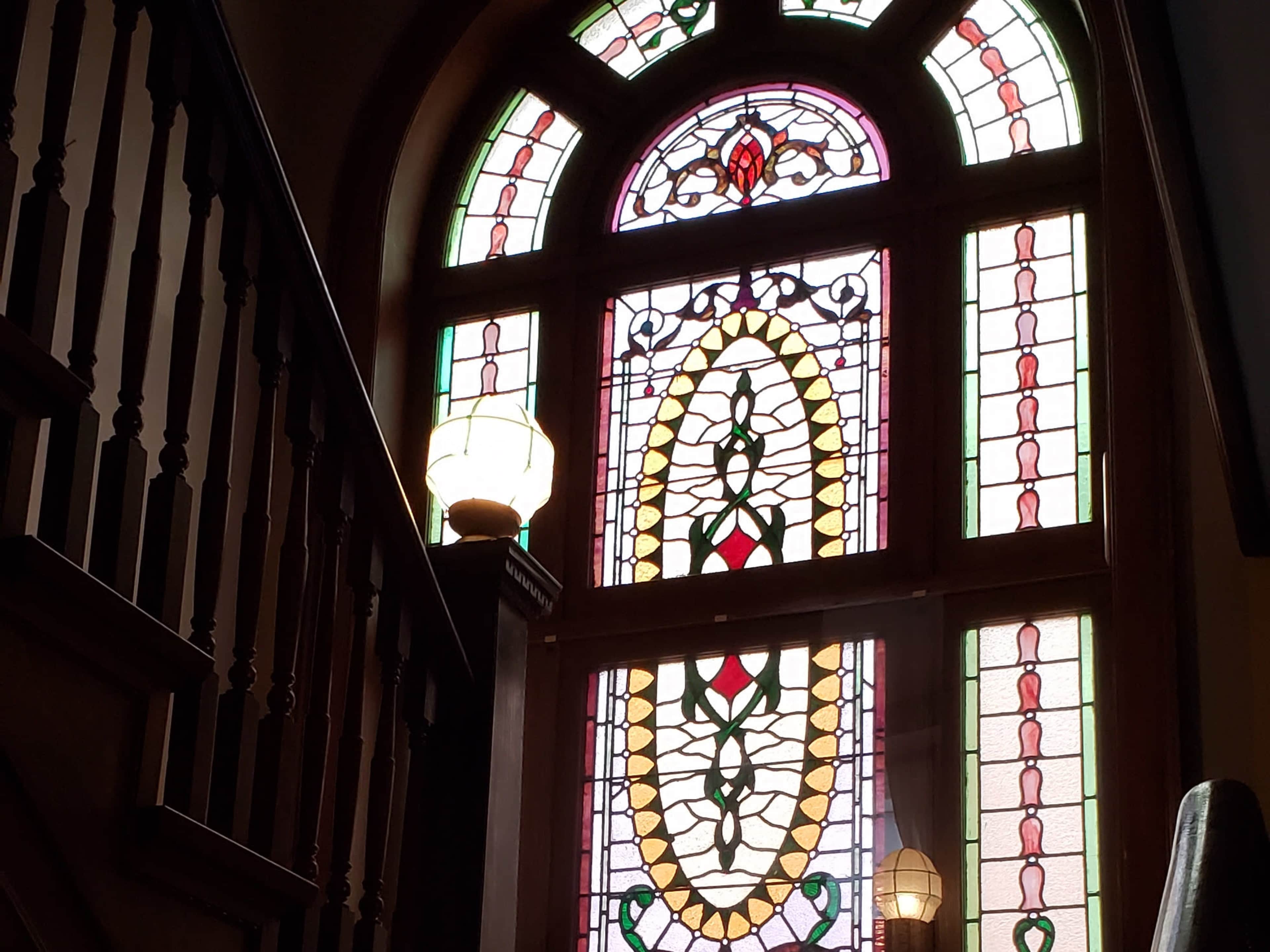 A staircase leading to an upper floor, with a large stained glass window featuring intricate patterns and colors.