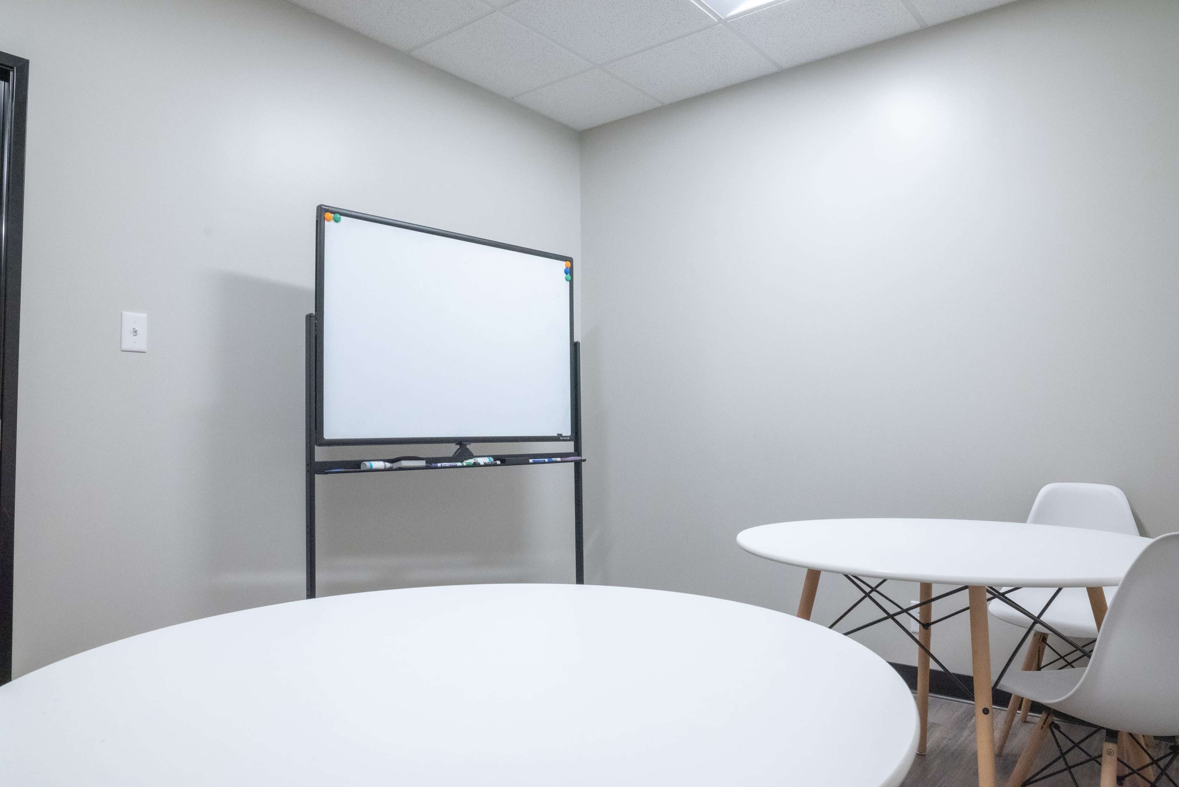A small meeting room features two round tables and a whiteboard on a stand against a wall.
