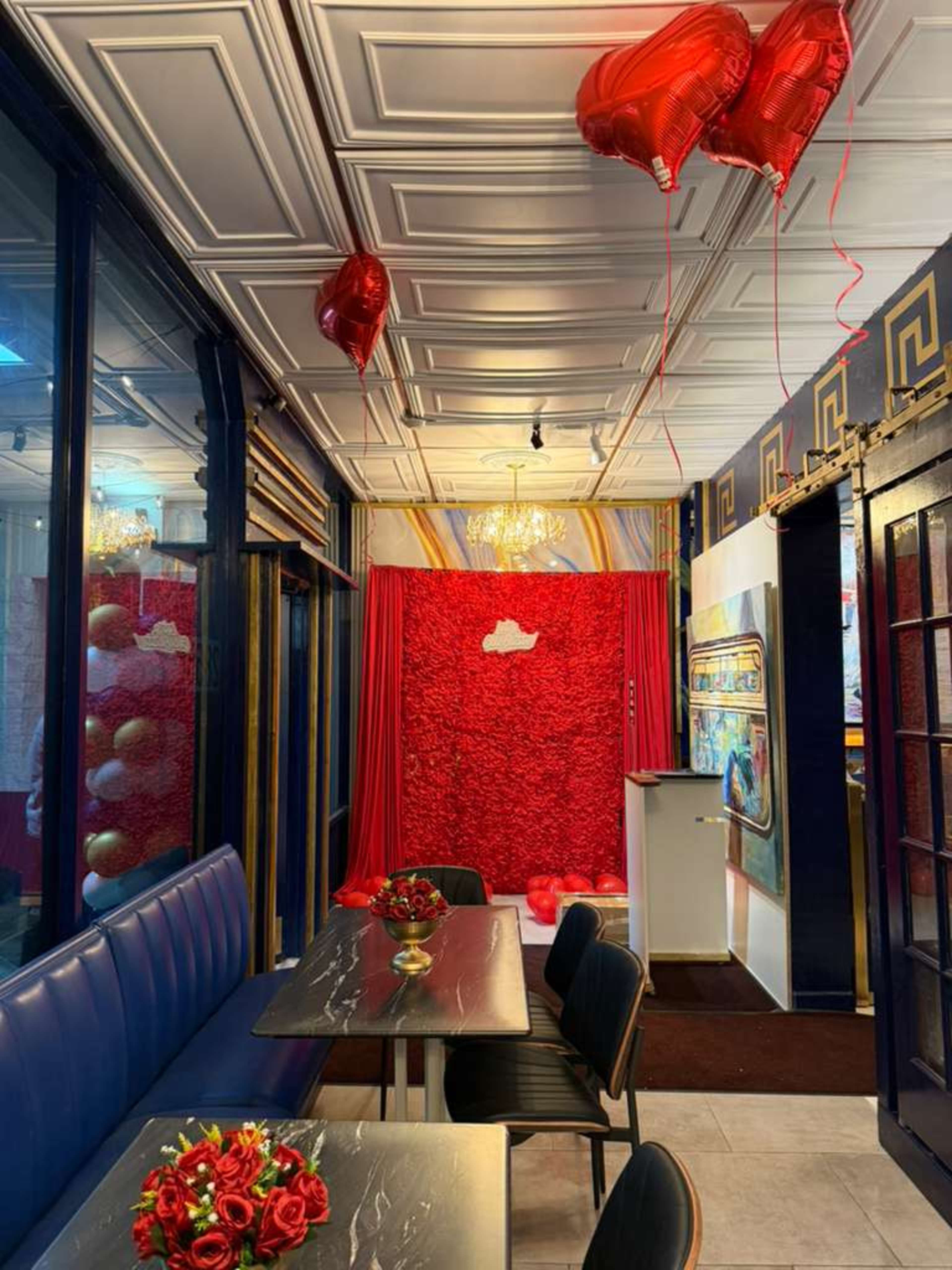 The interior of a restaurant features blue seating, red balloons, and a backdrop adorned with red flowers.