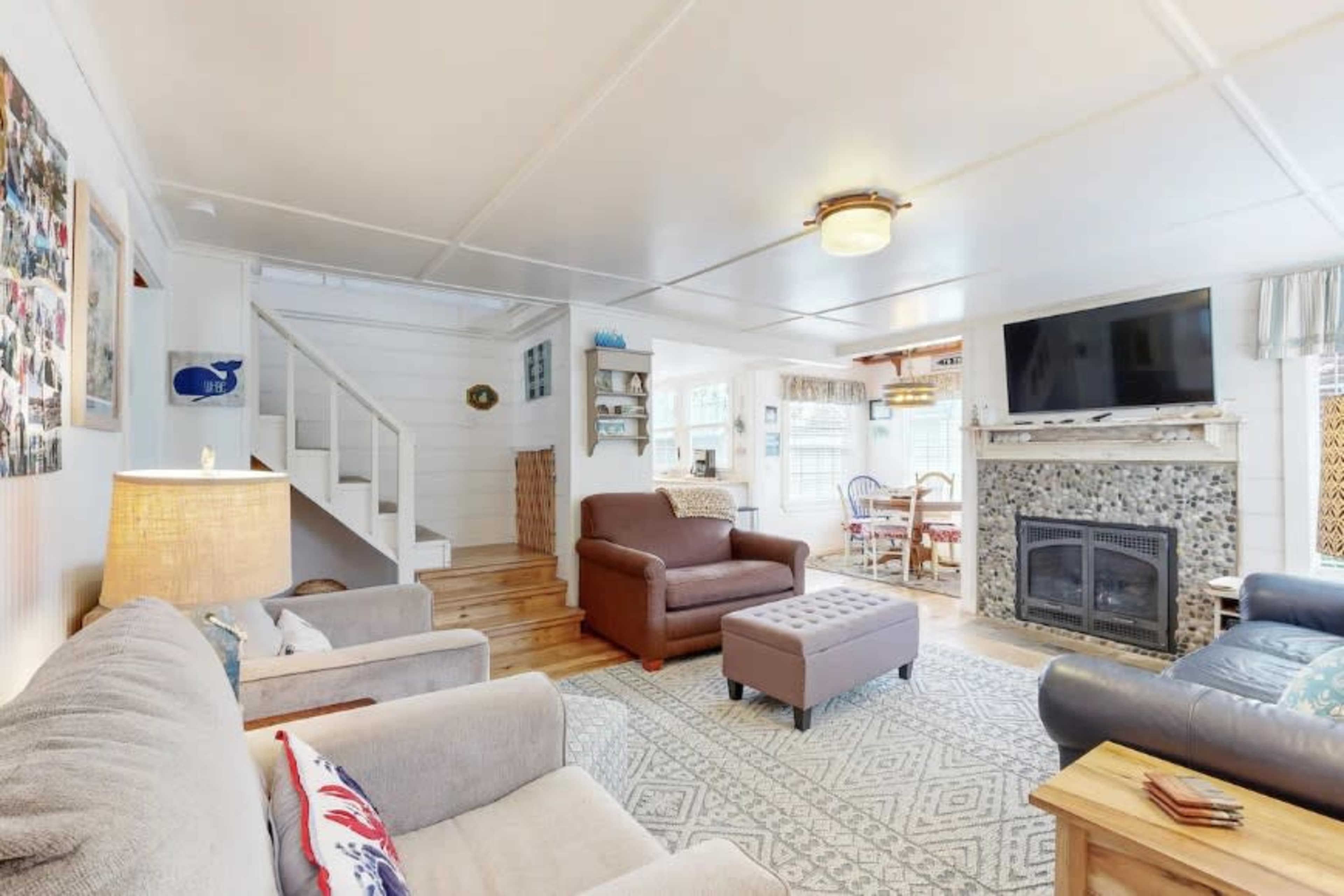 A cozy living room features a seating area with two sofas, a decorative rug, a stone fireplace, and a staircase leading to another level.
