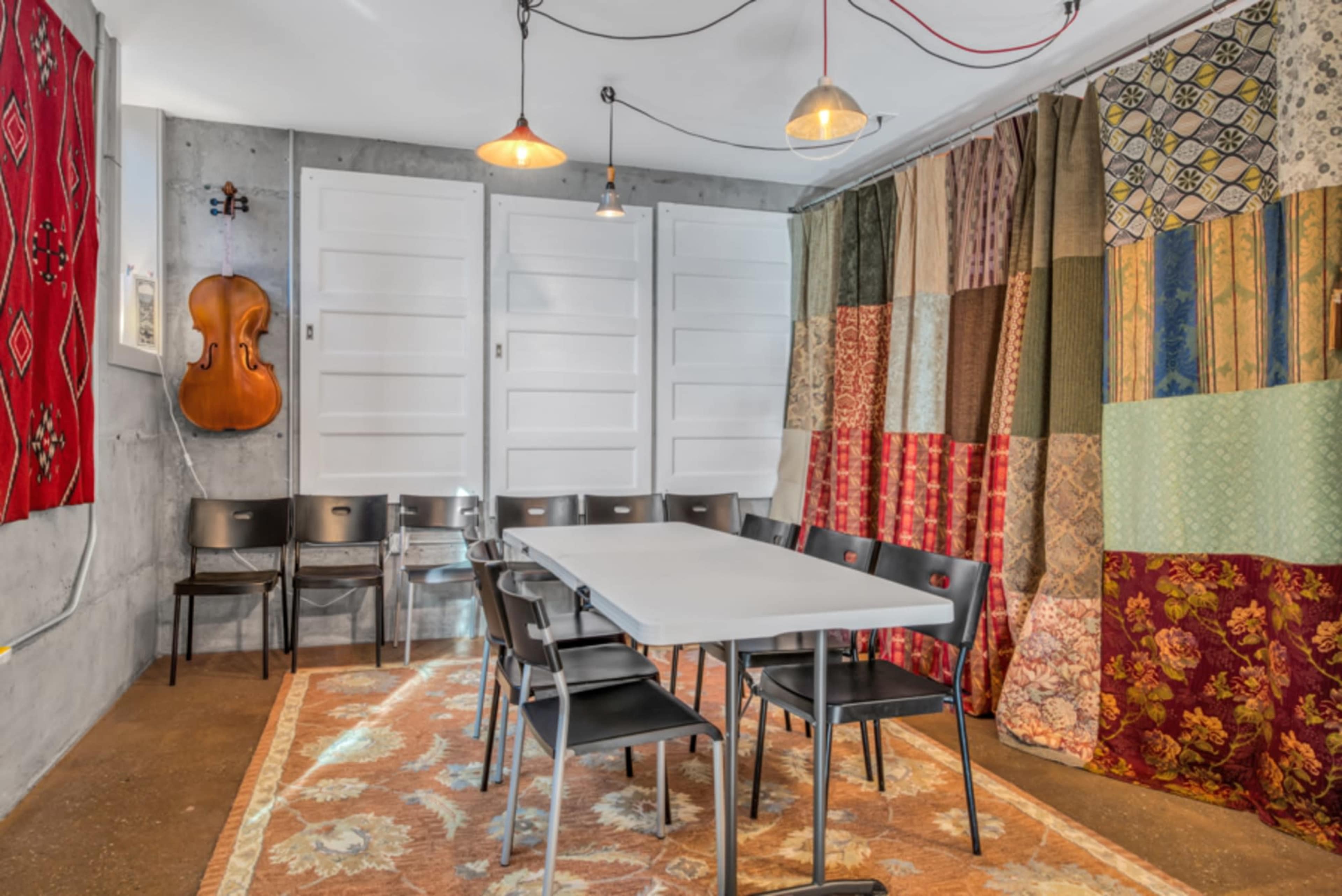 A small meeting room features a long table surrounded by black chairs, with colorful fabric drapes and a violin mounted on the wall.