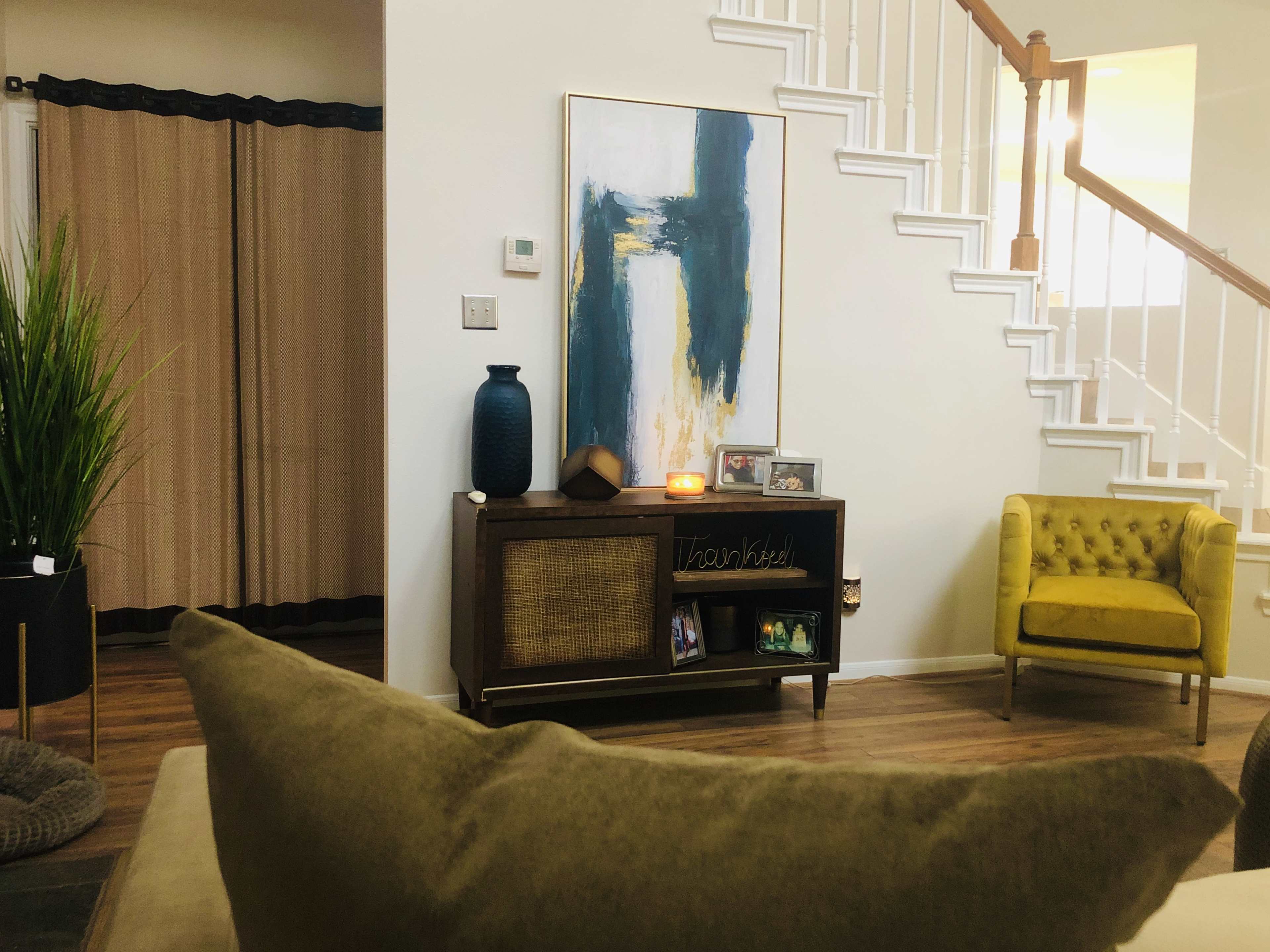 A cozy living room featuring a green sofa, a yellow armchair, a wooden console table with decor, and a large abstract painting on the wall.