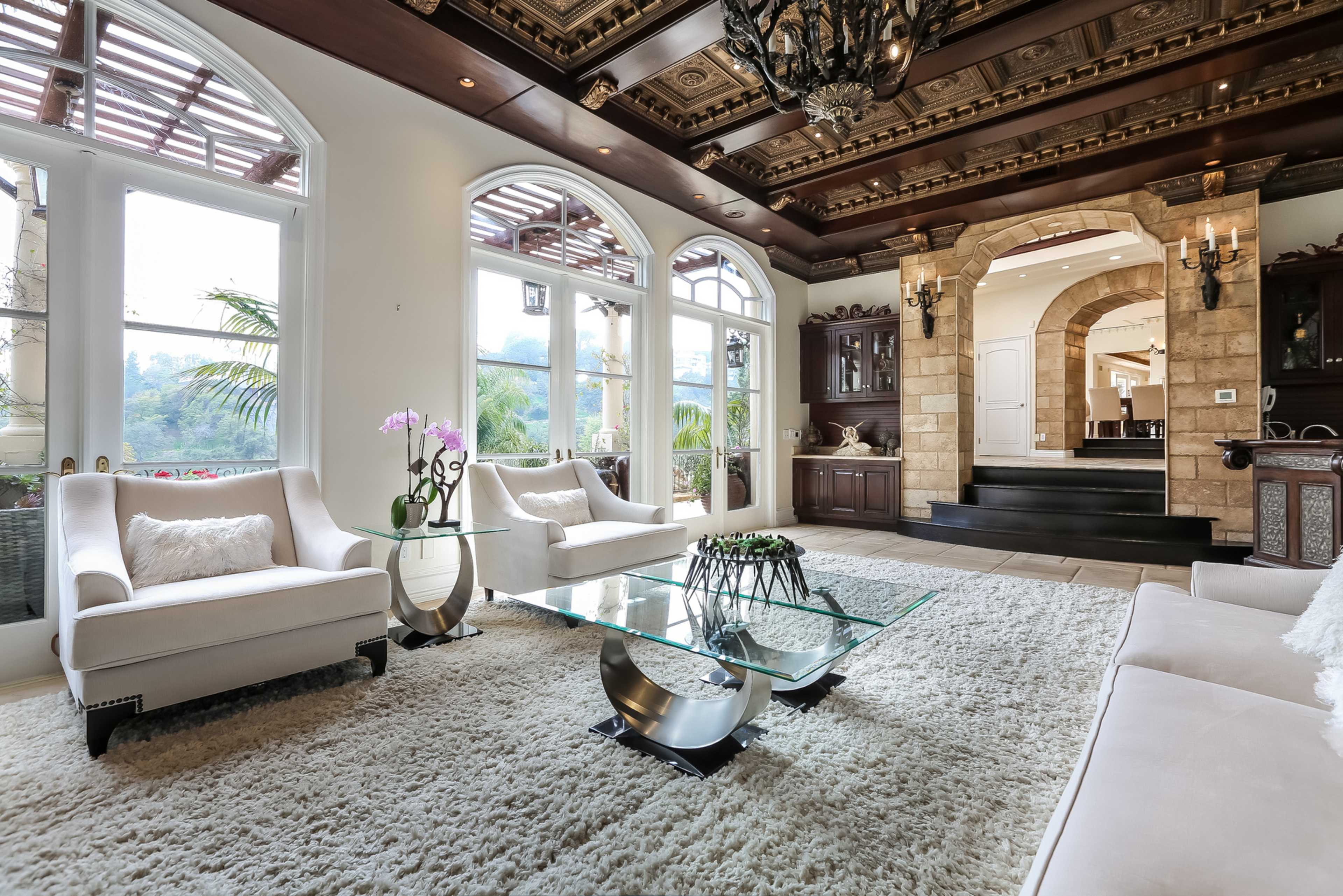 A spacious living room with elegant furnishings, a glass coffee table, and a decorative ceiling.