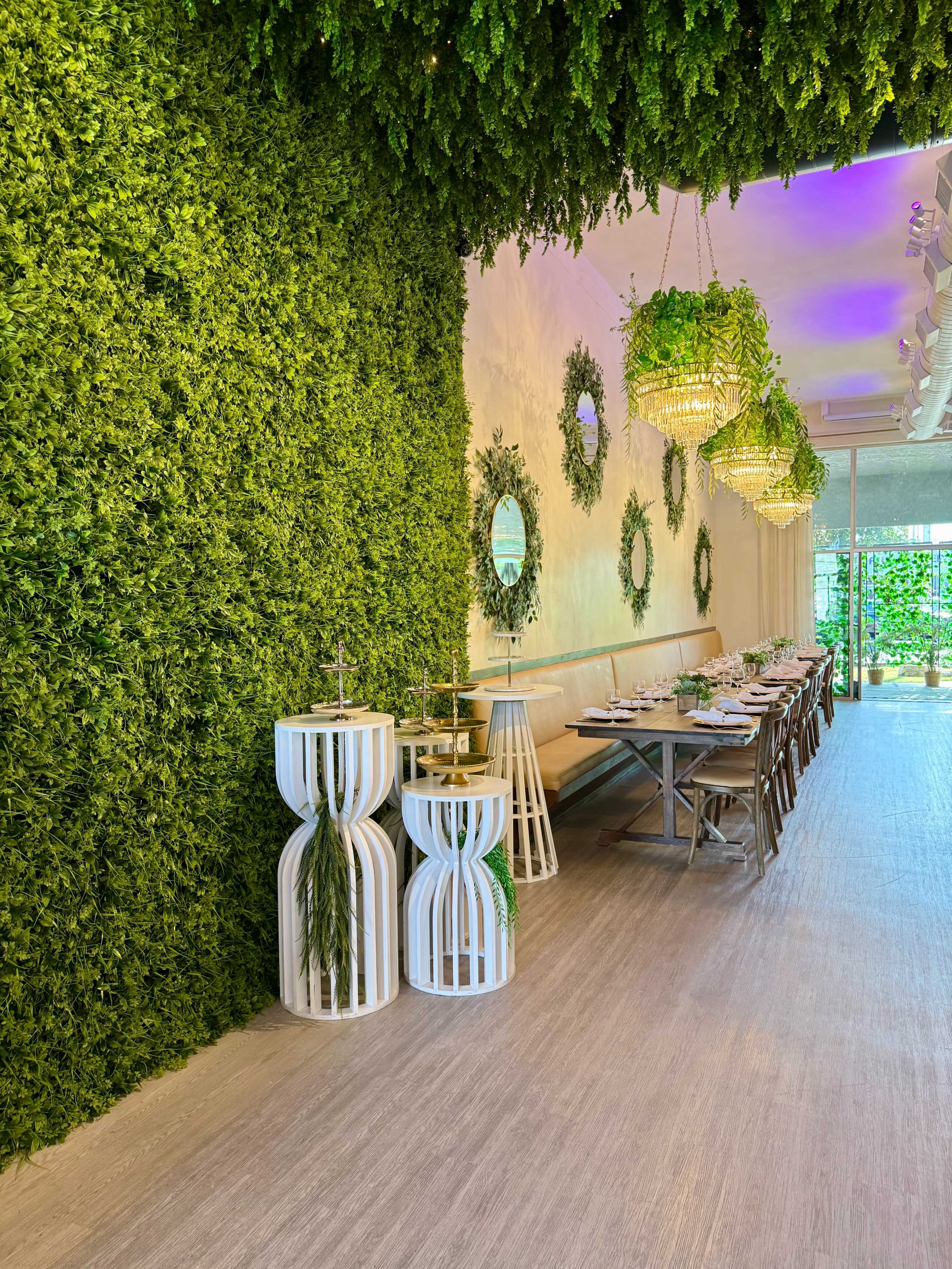 The image shows a dining area with a lush green wall, elegantly arranged tables, and decorative circular mirrors.