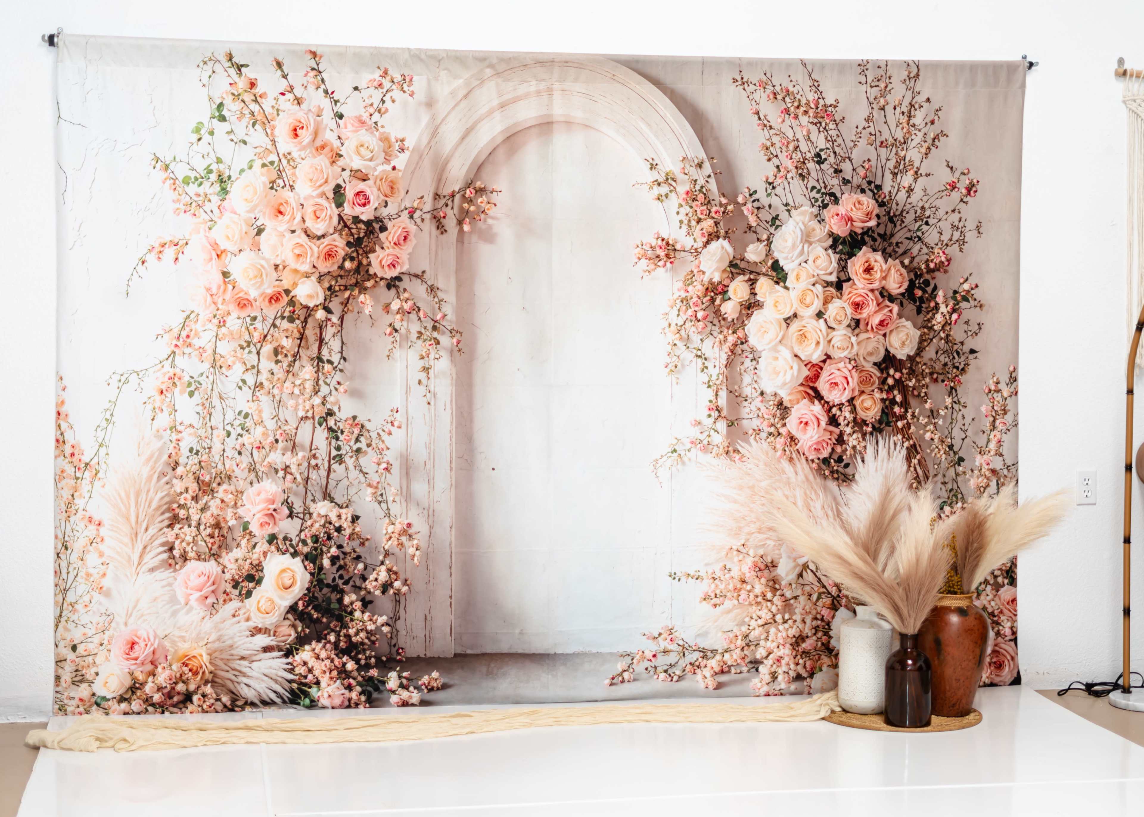 The image features a backdrop with an arch surrounded by a floral arrangement of pink roses and dried plants.