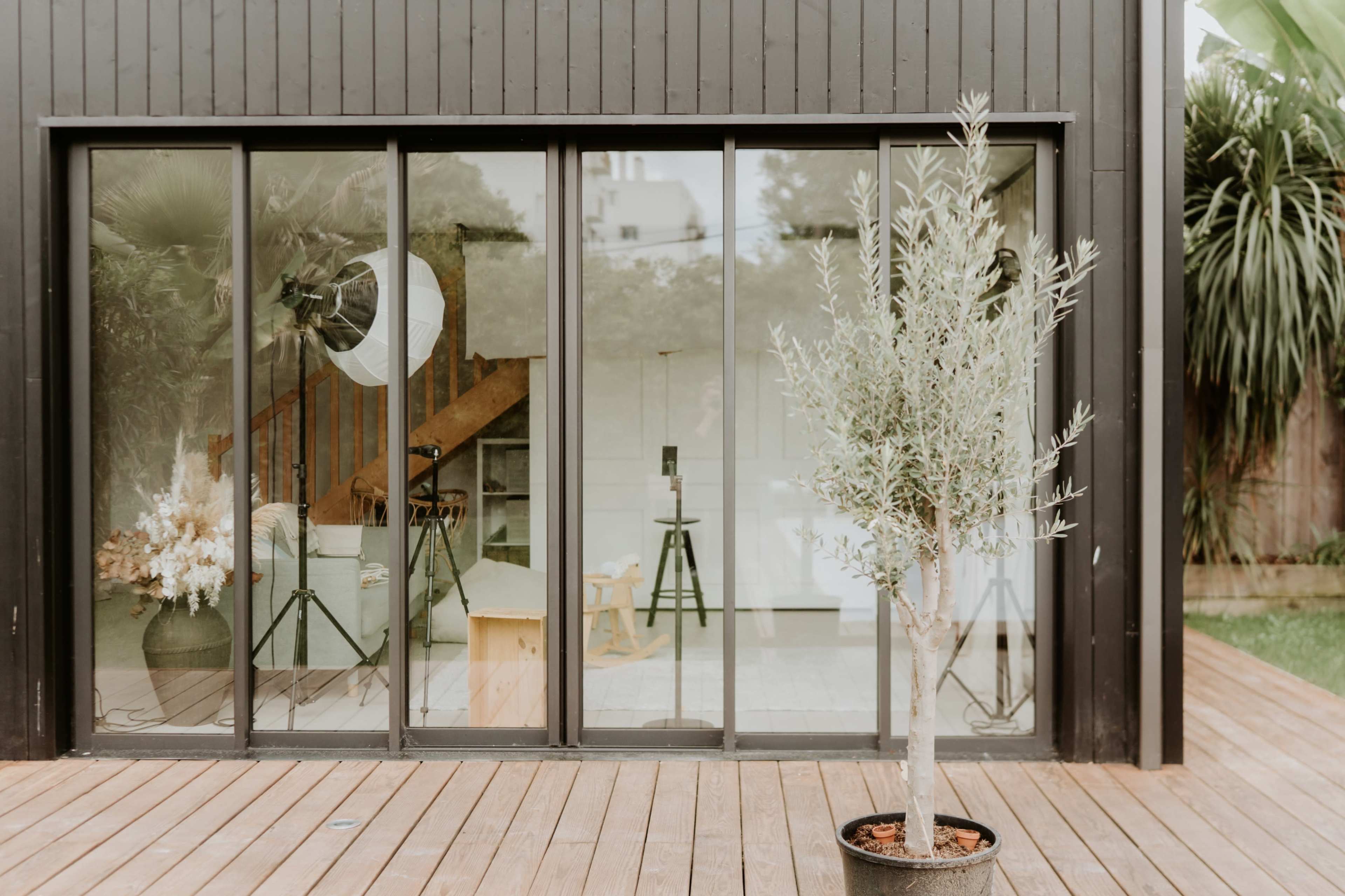 A modern black wooden building features large glass doors with a view of a bright interior and outdoor greenery.