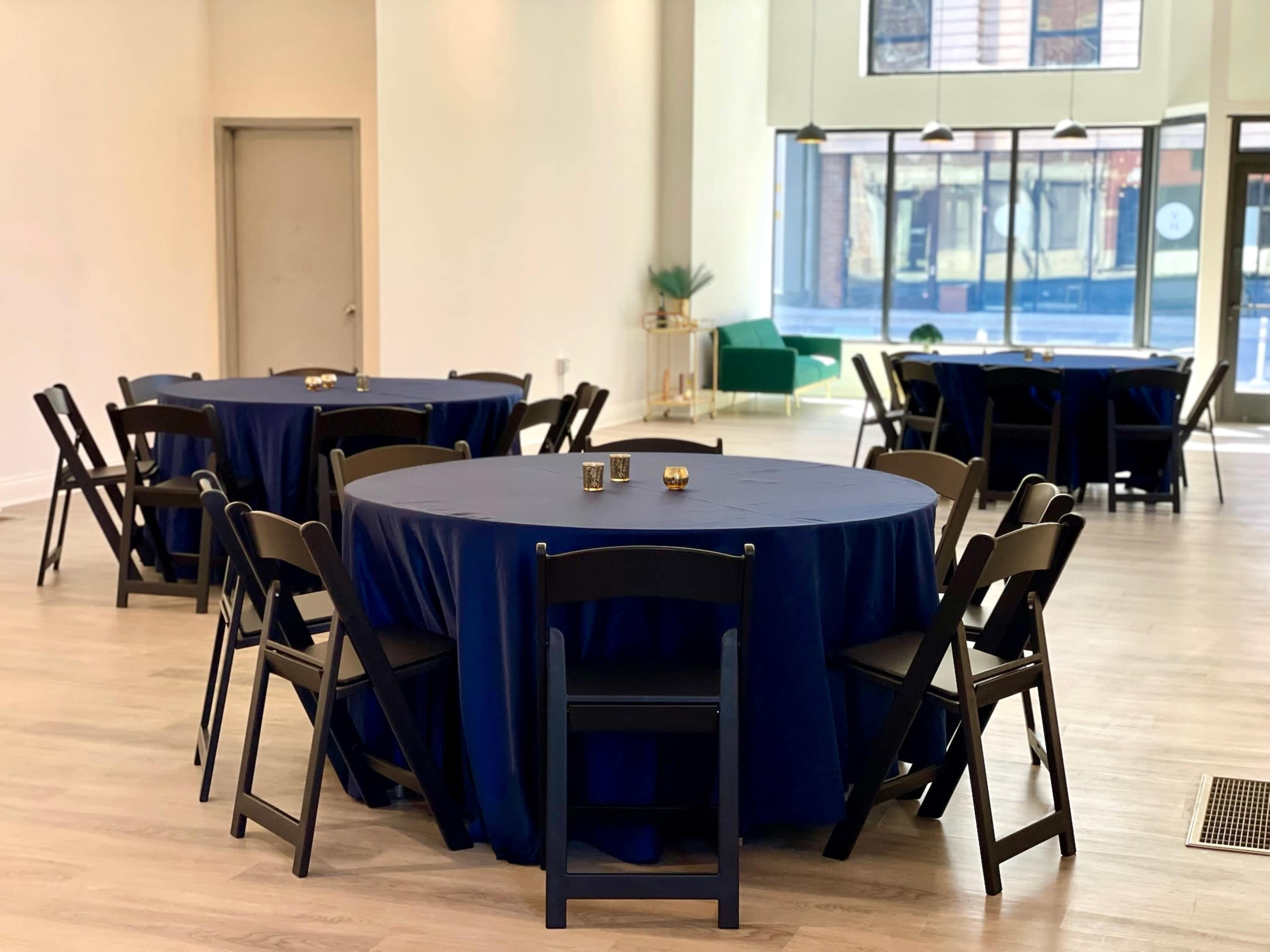 A spacious room with several round tables covered in navy tablecloths and surrounded by black chairs.