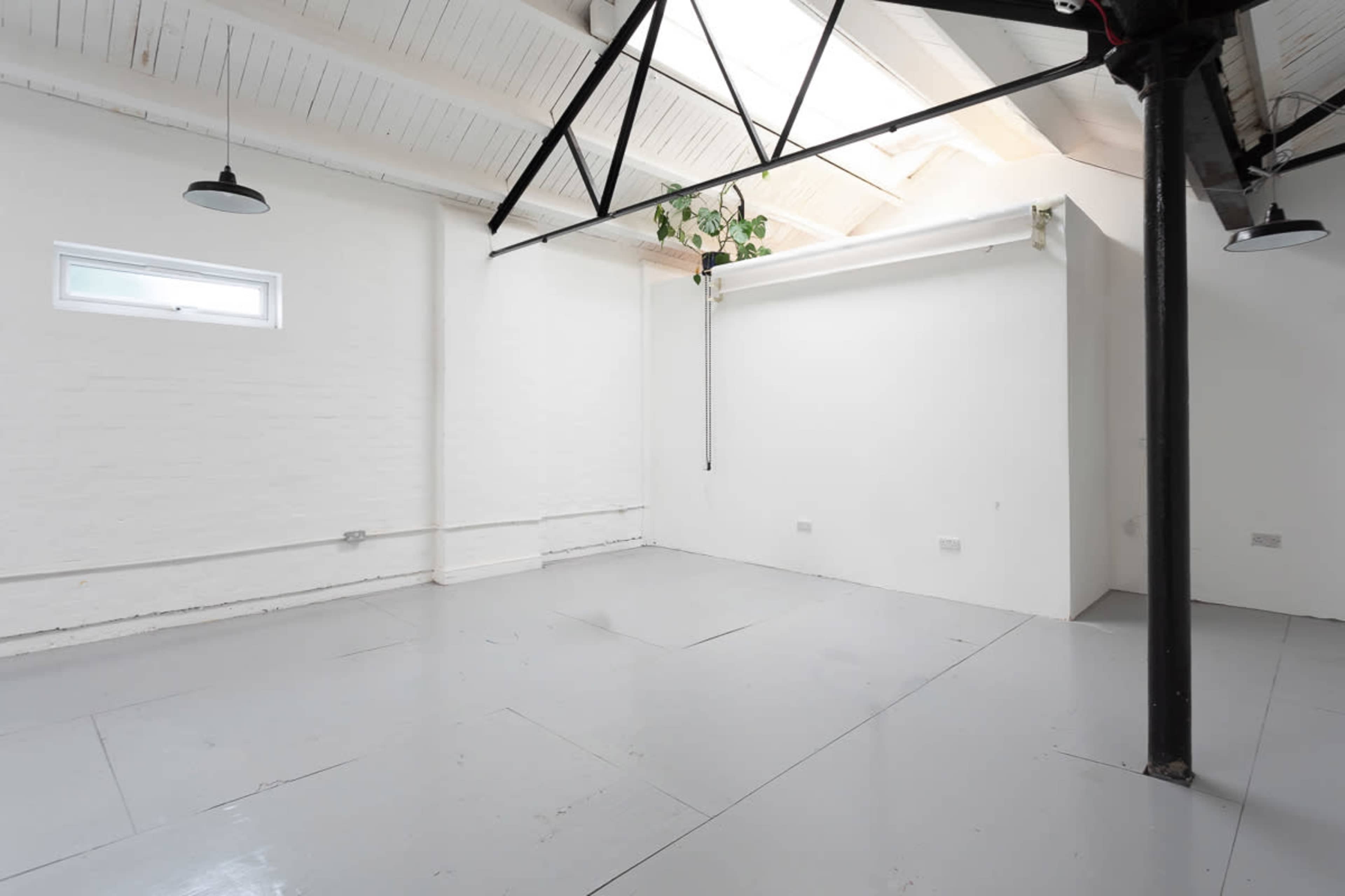 The image shows a spacious, brightly lit room with white walls, a gray floor, and overhead lights.