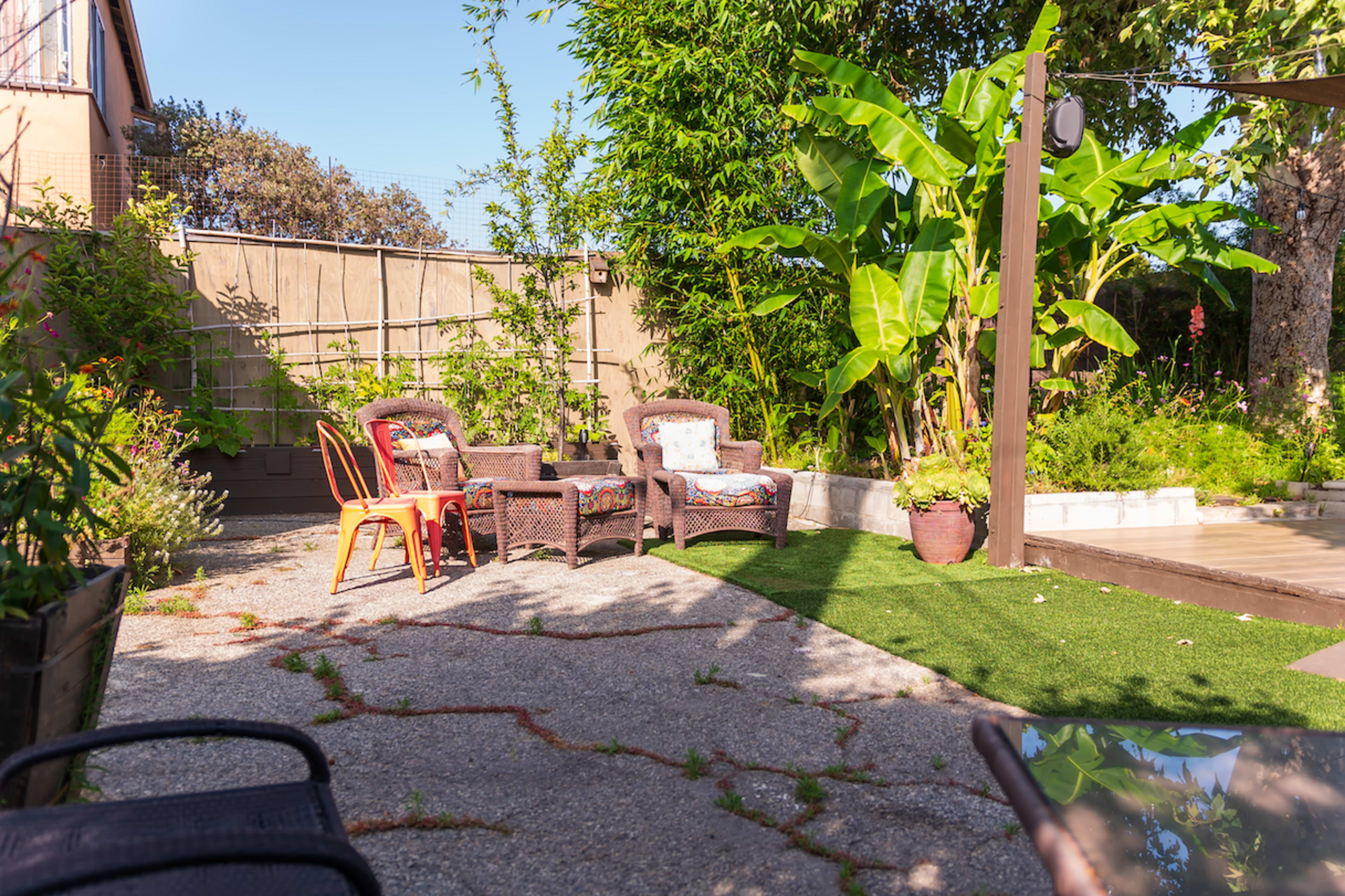 A cozy outdoor seating area features wicker chairs and a small table surrounded by greenery and a decorative wall.
