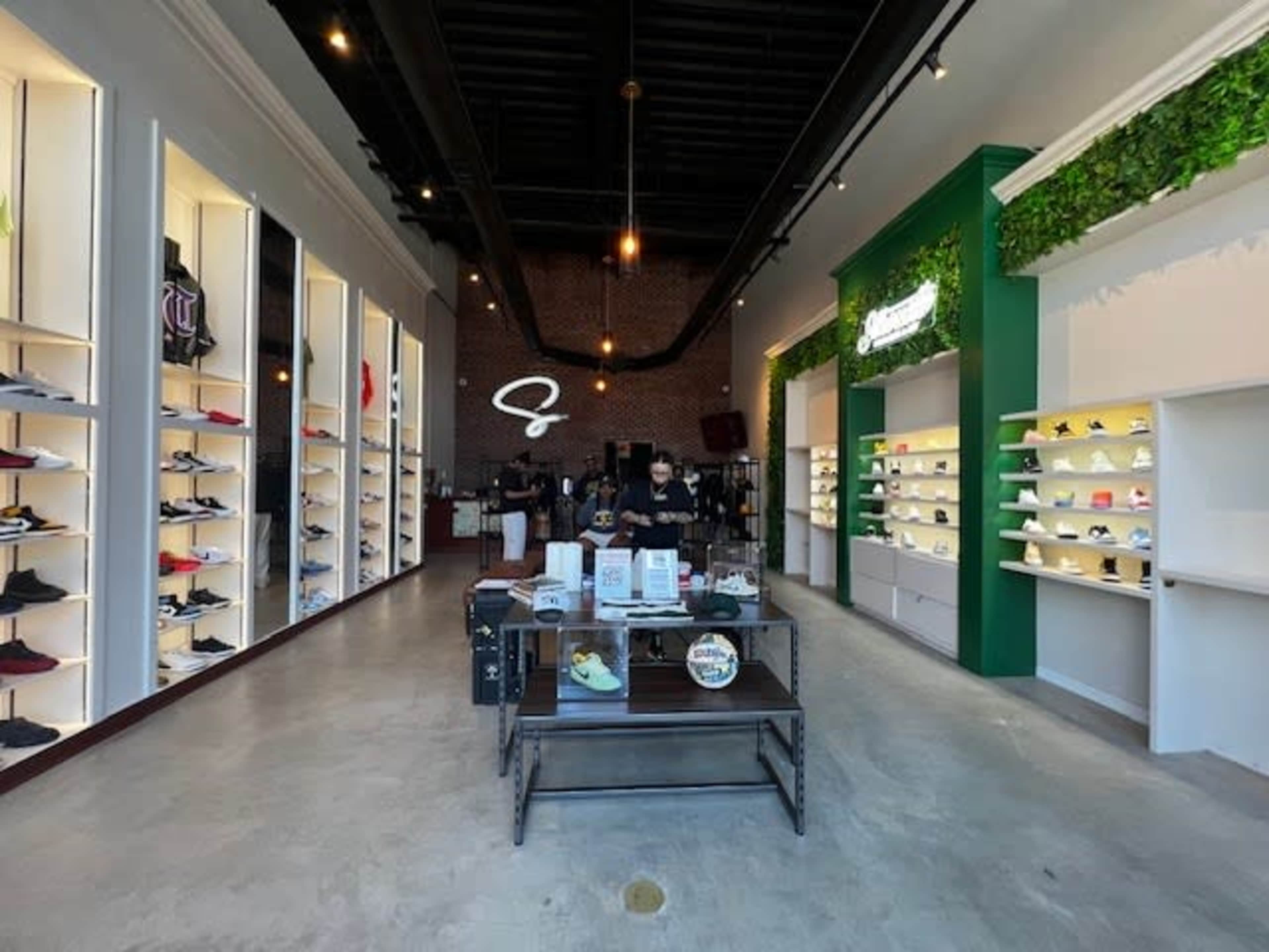 The interior of a shoe store features neatly organized shelves displaying various footwear, with a cashier's counter in the center of the space.
